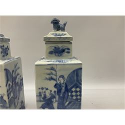 Pair of Chinese blue and white jars and covers of square form, decorated with figures in garden settings, the covers with foo dog finials, H21.5cm