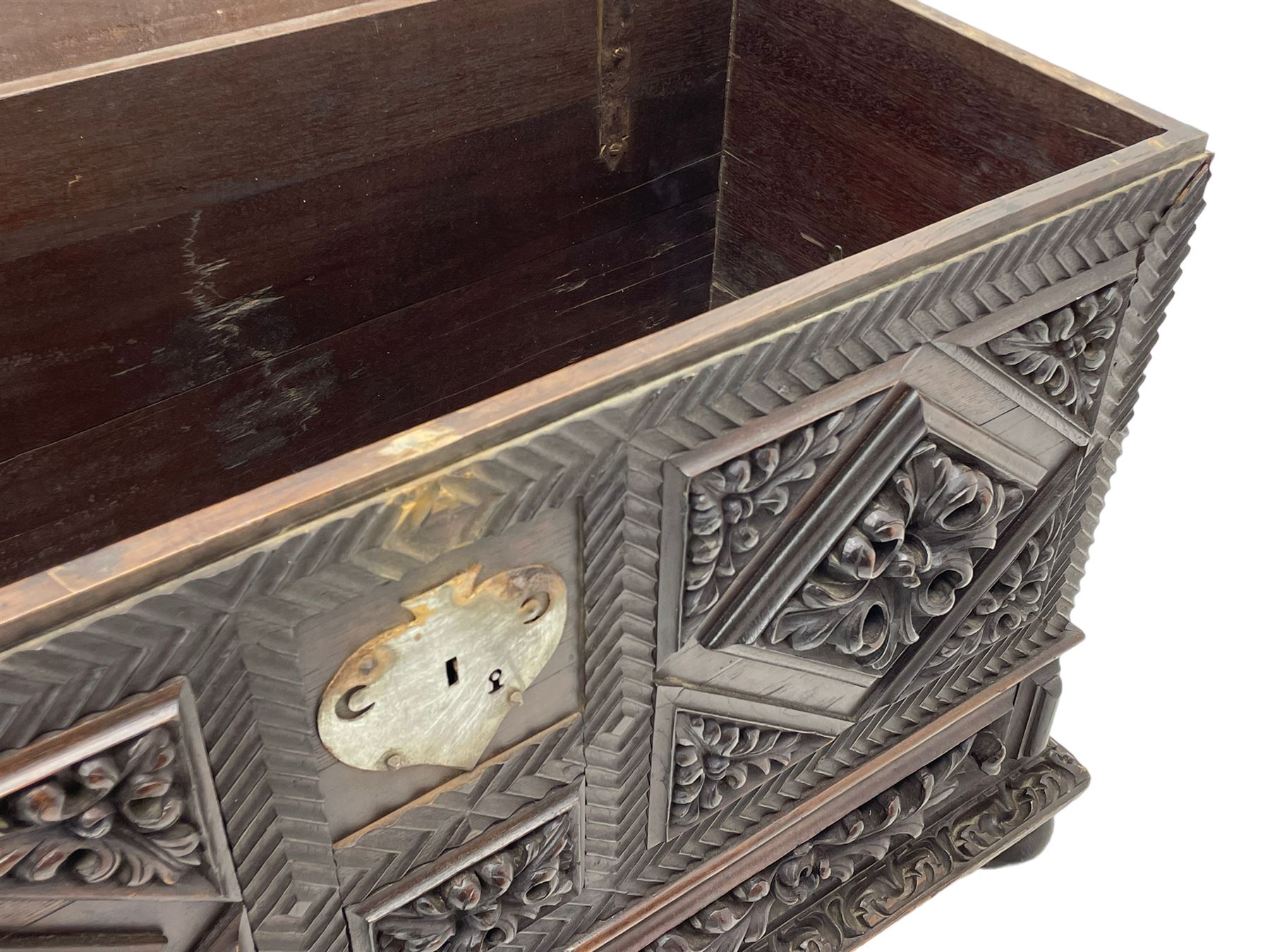 Early 20th century carved hardwood kist or mule chest of small proportions, moulded rectangular hinged lid over foliage carved geometric lozenge panels, the frame carved with chevron banding, fitted with two drawers, the drawer fronts carved with extending leaf motifs over a foliage carved lower moulding, on turned feet
