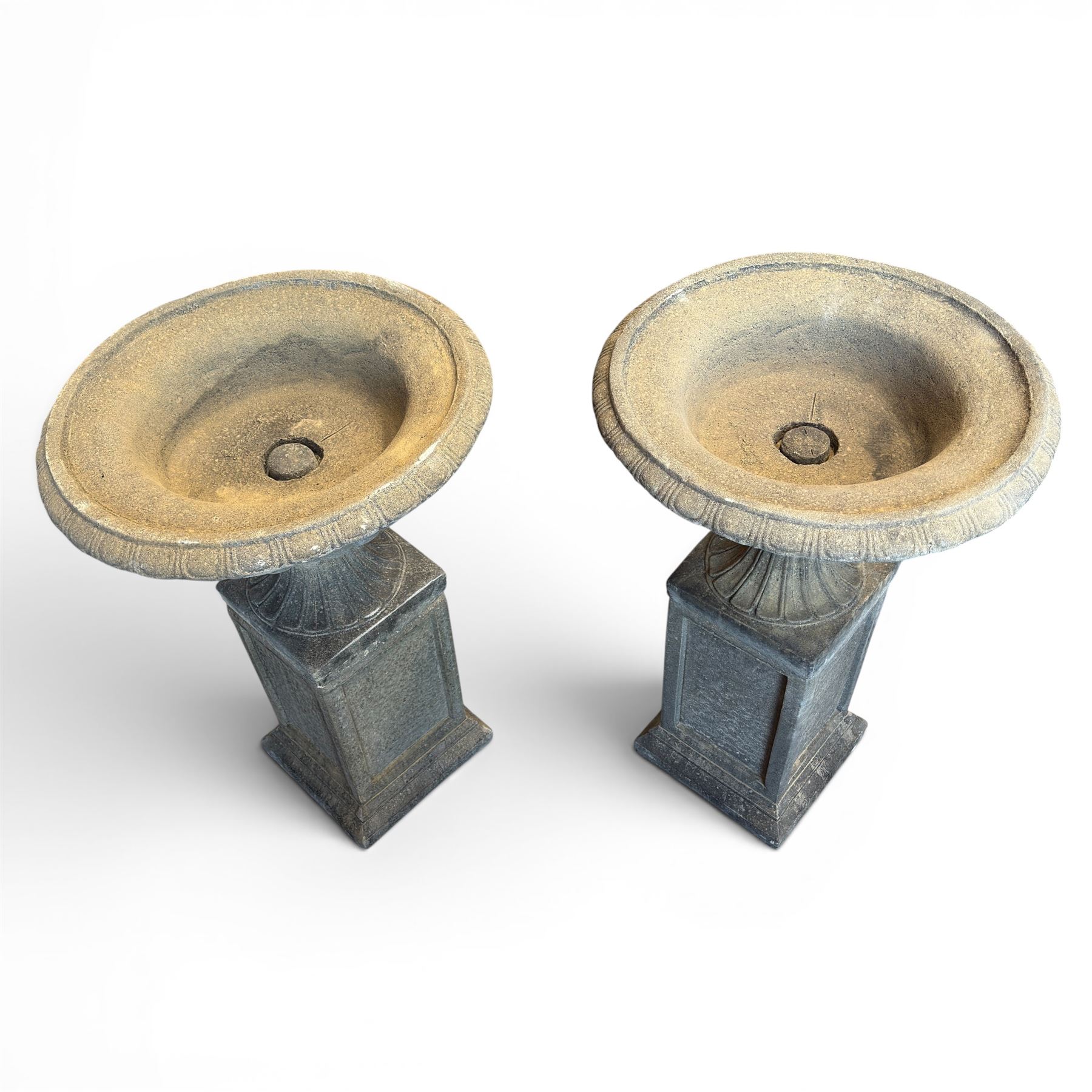 Pair of cast stone garden urns of kylix form on pedestals, the broad egg-and-dart moulded rim over a shallow gadrooned underbelly, with waisted tapering base, raised on matching plinth bases with faux panelled facia