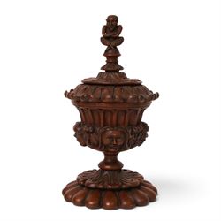 Carved wooden urn. decorated in relief with carved faces within foliage, with a Satyr finial, H25cm 