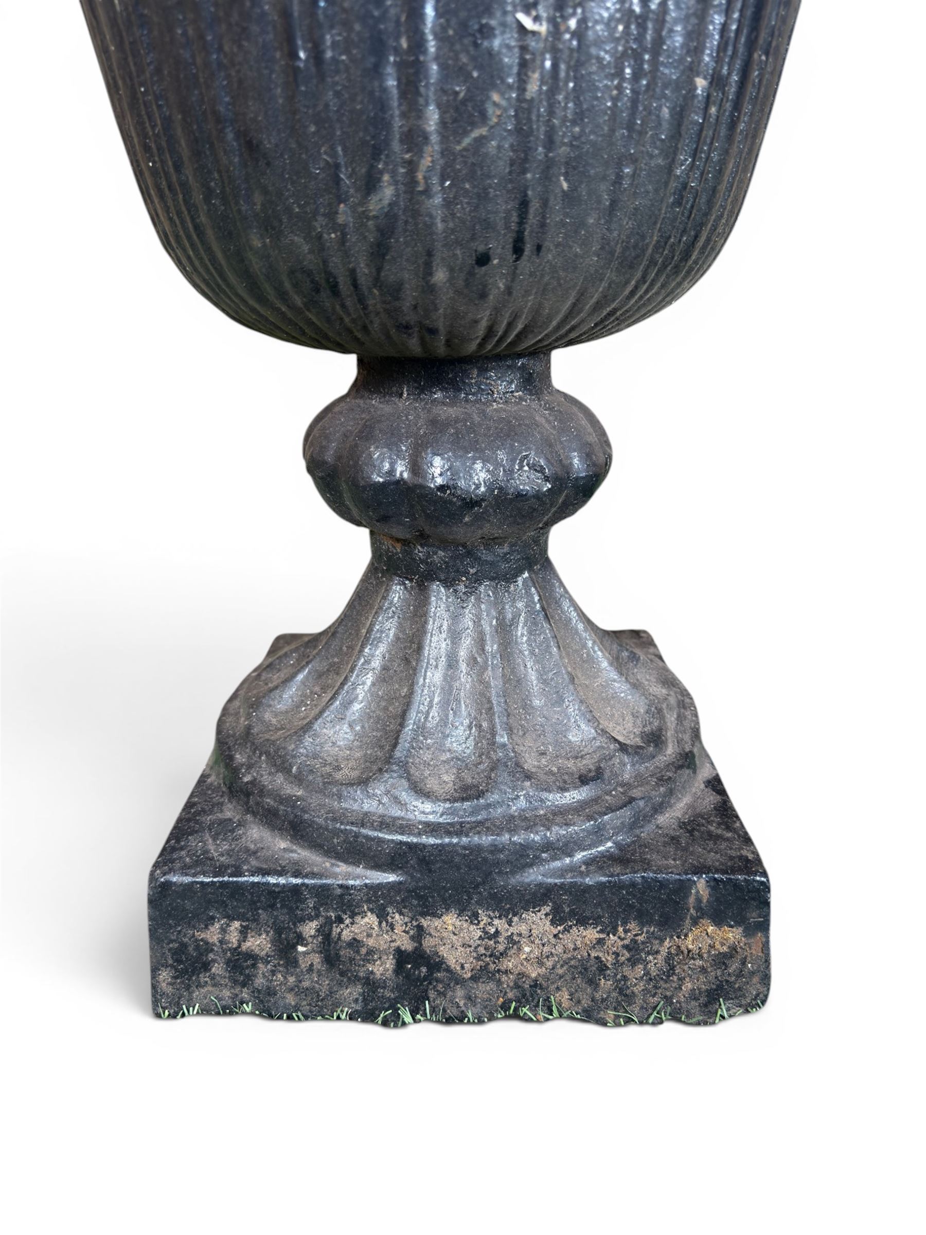 Pair of Victorian large scale cast iron garden urns, flared petal shaped rim with tapering waist, gadrooned base on square plinth, finished in black paint