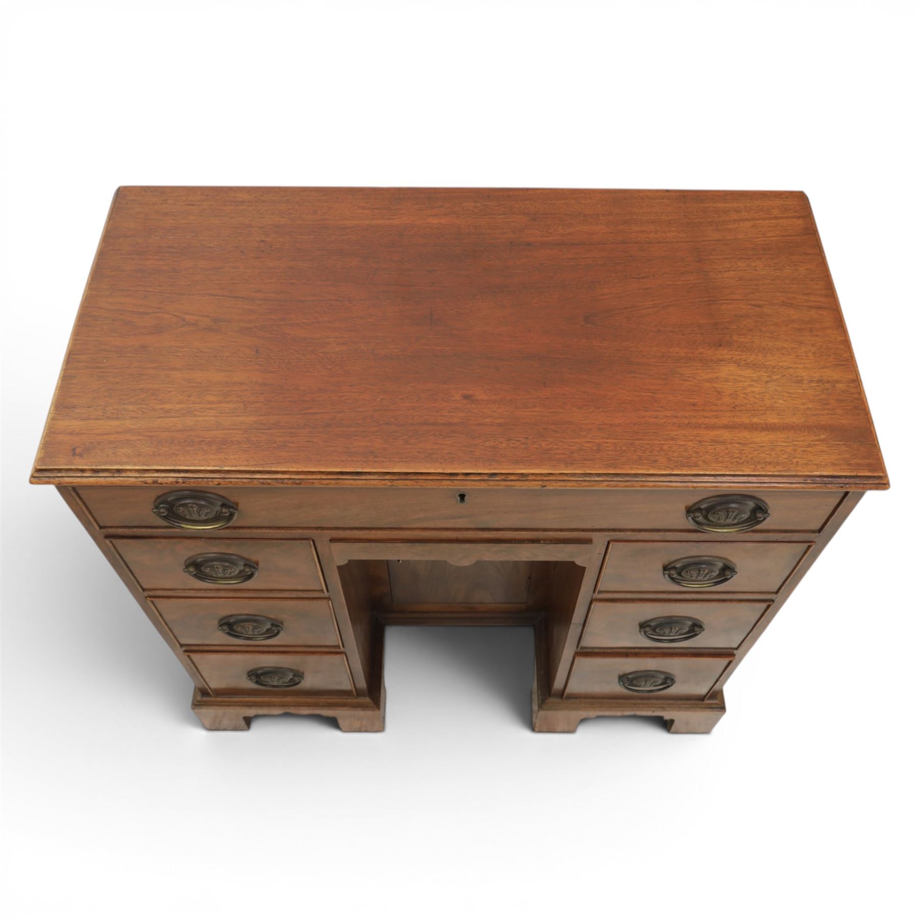 Early 20th century Georgian design figured walnut kneehole desk, rectangular moulded top over one long frieze drawer, kneehole recess with cupboard and drawer above, flanked by six short drawers with oval pressed brass handle plates, moulded plinth base on bracket feet