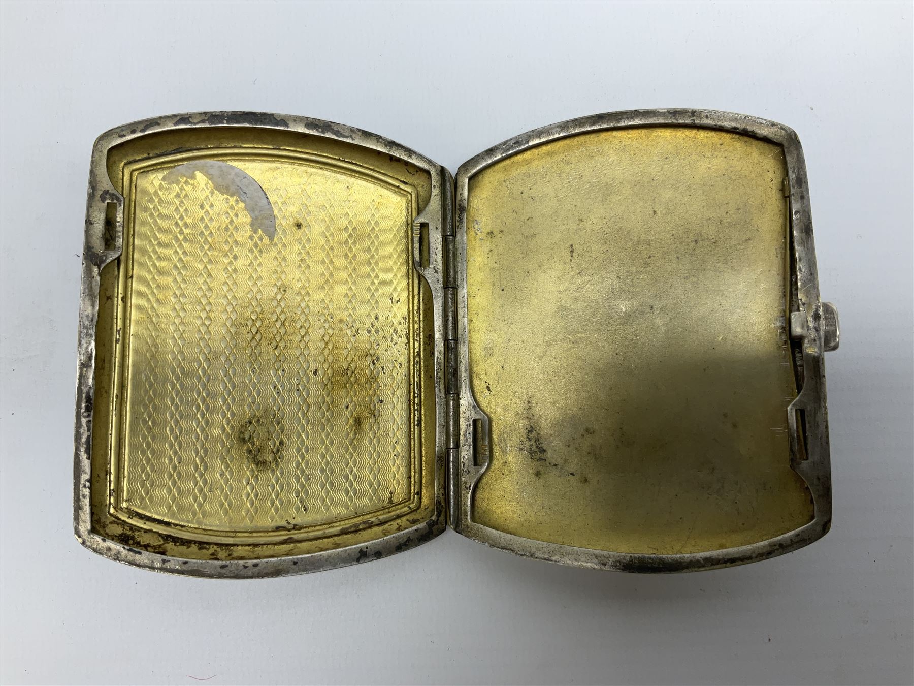 Early 20th century Continental erotic cigarette case, the silver-plate body of curved rectangular form with cover decorated with painted enamel street scene depicting young boy in squatting position lighting a cigarette shielded from the wind by his girlfriend, who is lifting the skirt of her dress up over him, with gilt interior, L9cm