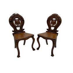 Pair late 19th century mahogany hall chairs, carved and pierced back with central shield surrounded by scrolling, serpentine shaped seat raised on scrolled cabriole supports