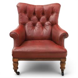 Early 20th century style oxblood red leather Chesterfield armchair, deep buttoned shaped back over padded scroll arms and loose seat cushion, raised on turned mahogany front supports with brass caps and castors