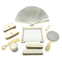 Early 20th century ivory dressing table set, comprising small footed tray with glass centre, handheld mirror, two hair brushes, two clothes brushes, cylindrical toothpick/pin case, stud jar, and shoe horn, plus a papier-mâché cased carved and pierced ivory fan