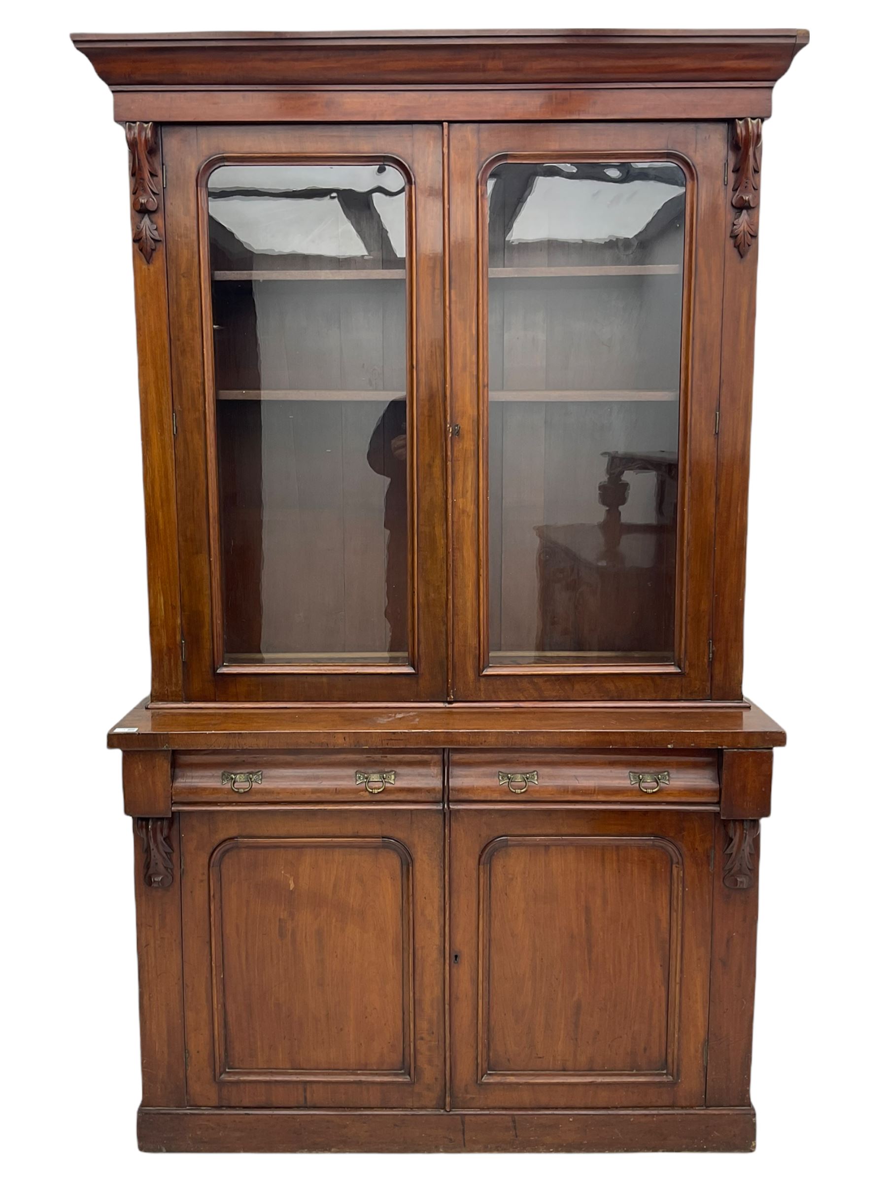 Victorian mahogany bookcase on cupboard, projecting cornice over two glazed doors and carved corbels, fitted with two drawers and double cupboard, plinth base