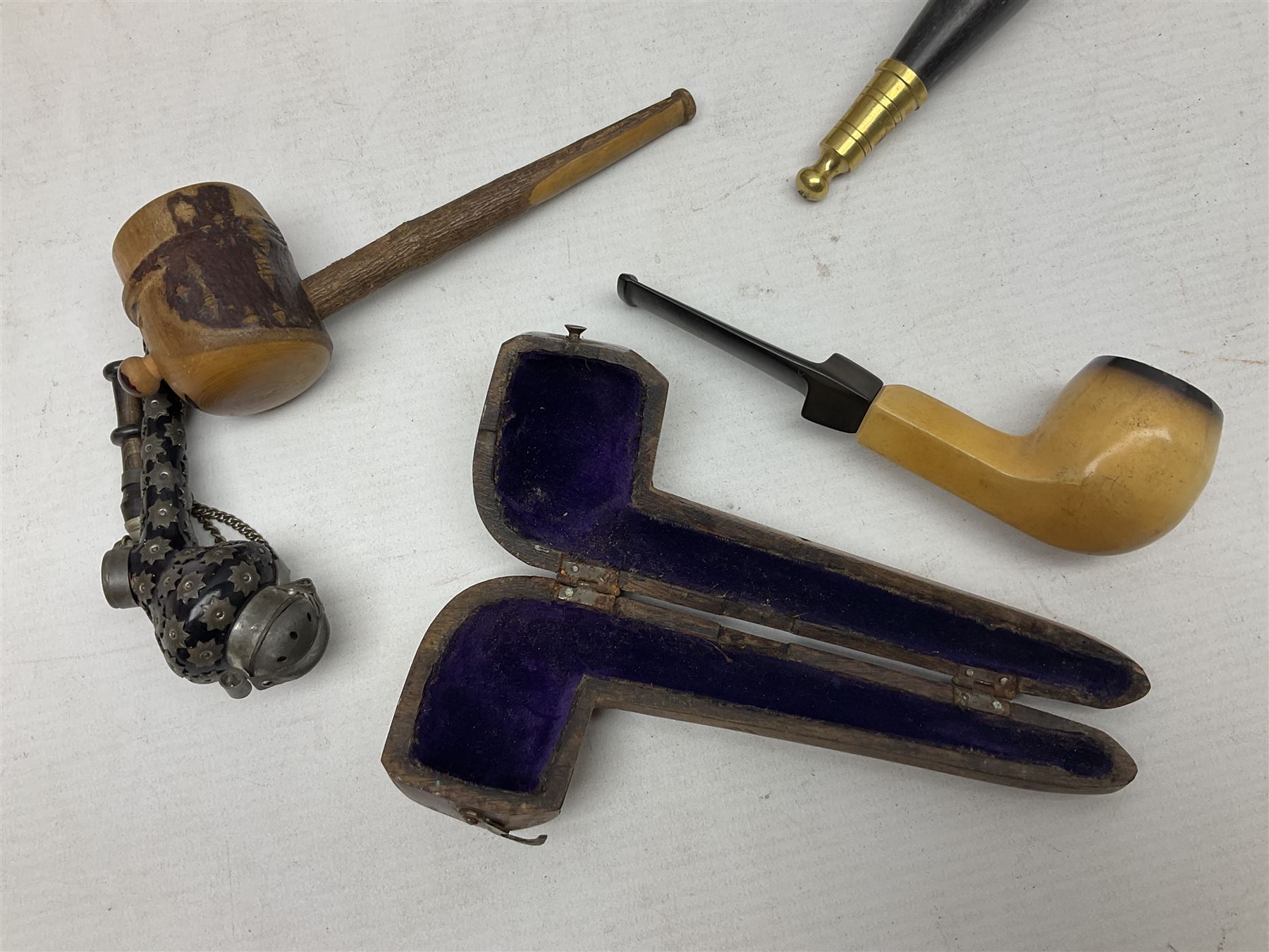 Swiss mountain hunters tobacco pipe with a horn mouthpiece, metal hinged pierced lid and brass chain, the black coated body adorned with small metal cow flowers, together with two other pipes and case, brass mounted horn, brass mounted bone box, carved mother of pearl handled knife and fork and brass jug