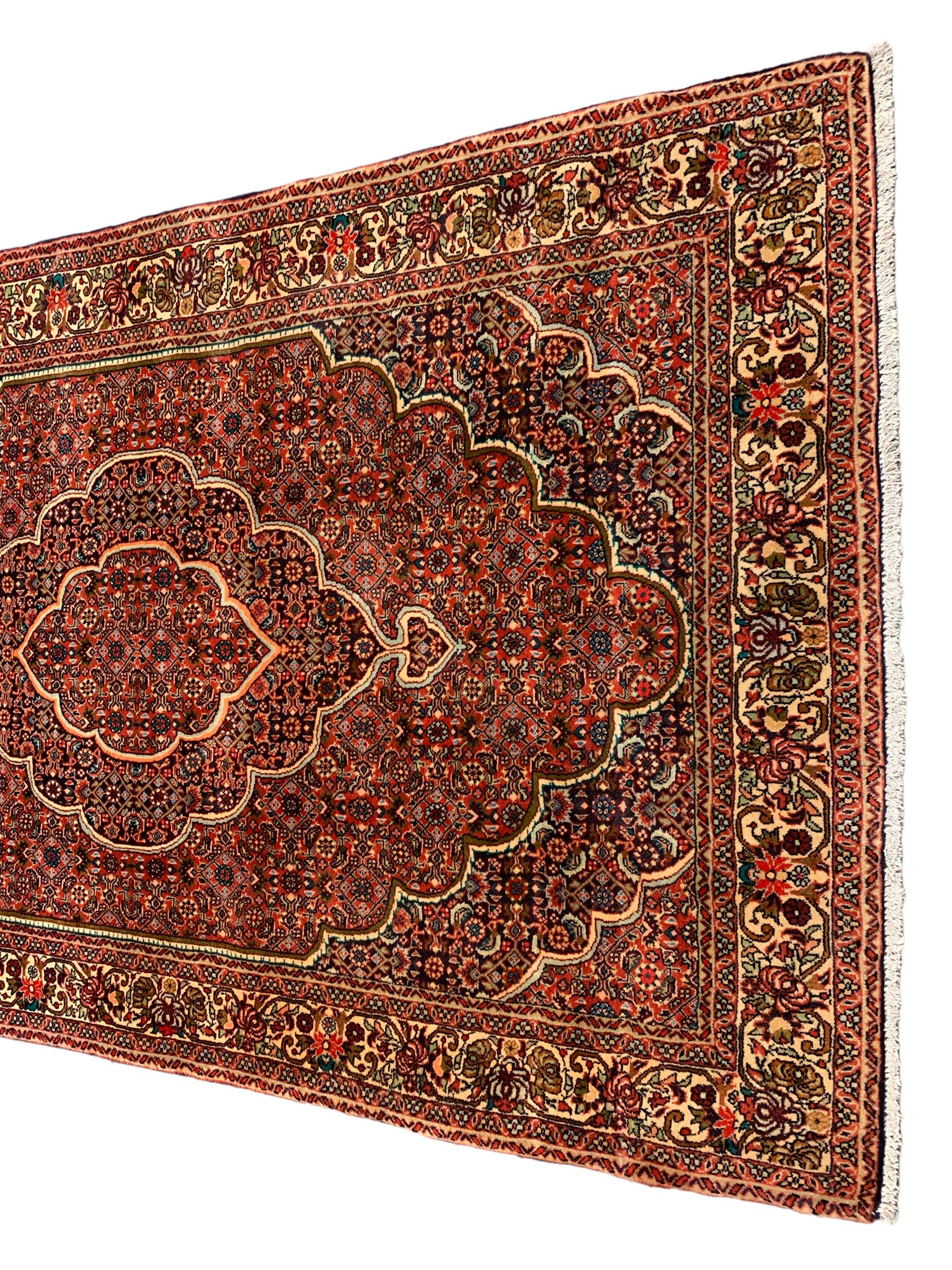 Persian Bidjar crimson ground rug, thick woollen pile, the field decorated with repeating Herati motifs within cusped outlines, the guarded border decorated with repeating flower head motifs
