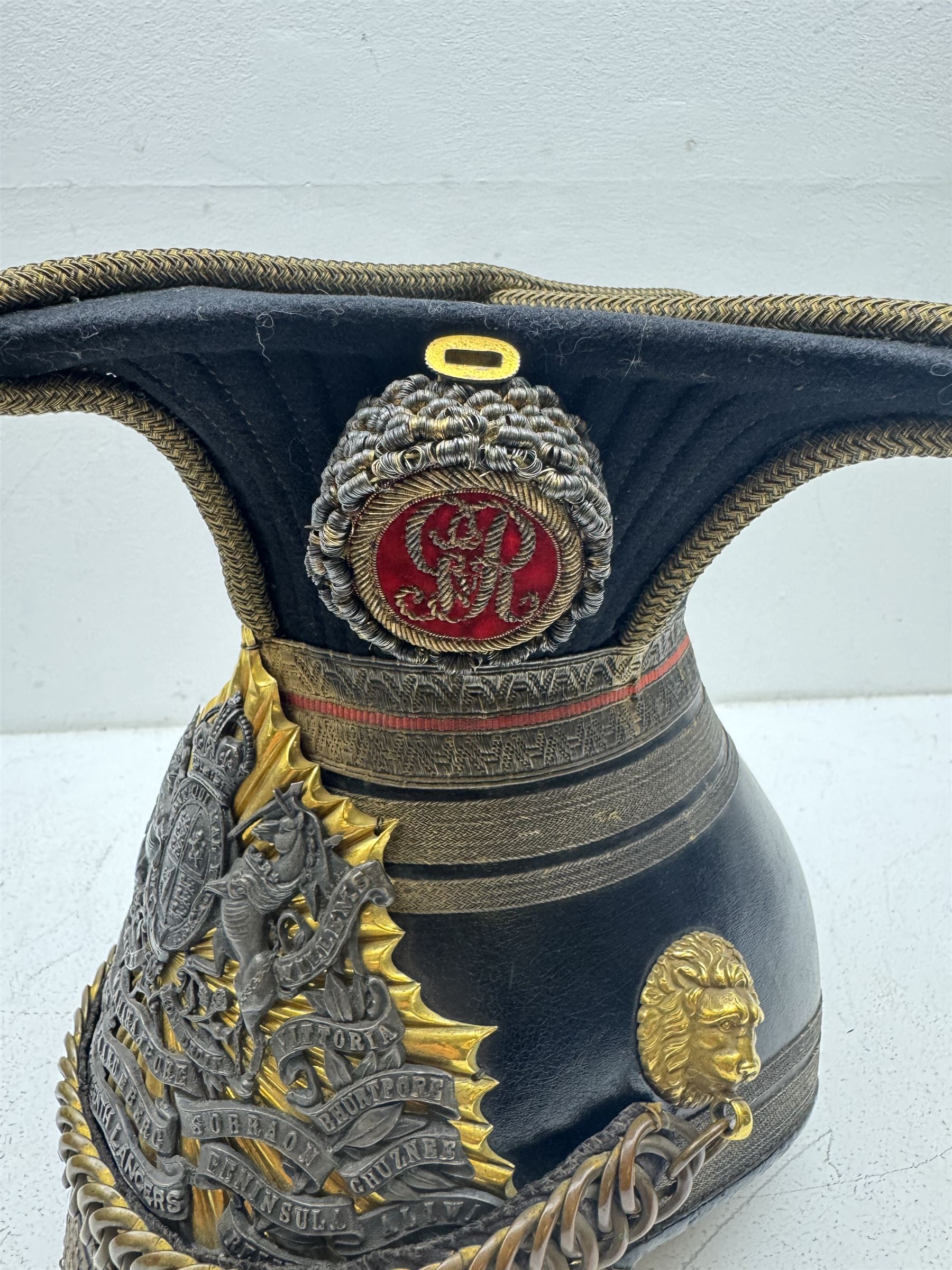 16th Queens Lancers Officers Lance Cap, black leather body with gilt braid lace and gilt wire braiding to the peak, officers silver gilt helmet plate to the front, the black cloth mortar board top with thick bullion wire, the bullion socket holder with embroidered GR cipher to the centre, lion head side bosses with velvet backed linked chinstrap, interior with leather sweatband and cloth lining, marked Carter & Co Pall Mall, the helmet is housed in japanned storage tin with brass plaque engraved “Lieu H L Evans, 16th Lancers'
