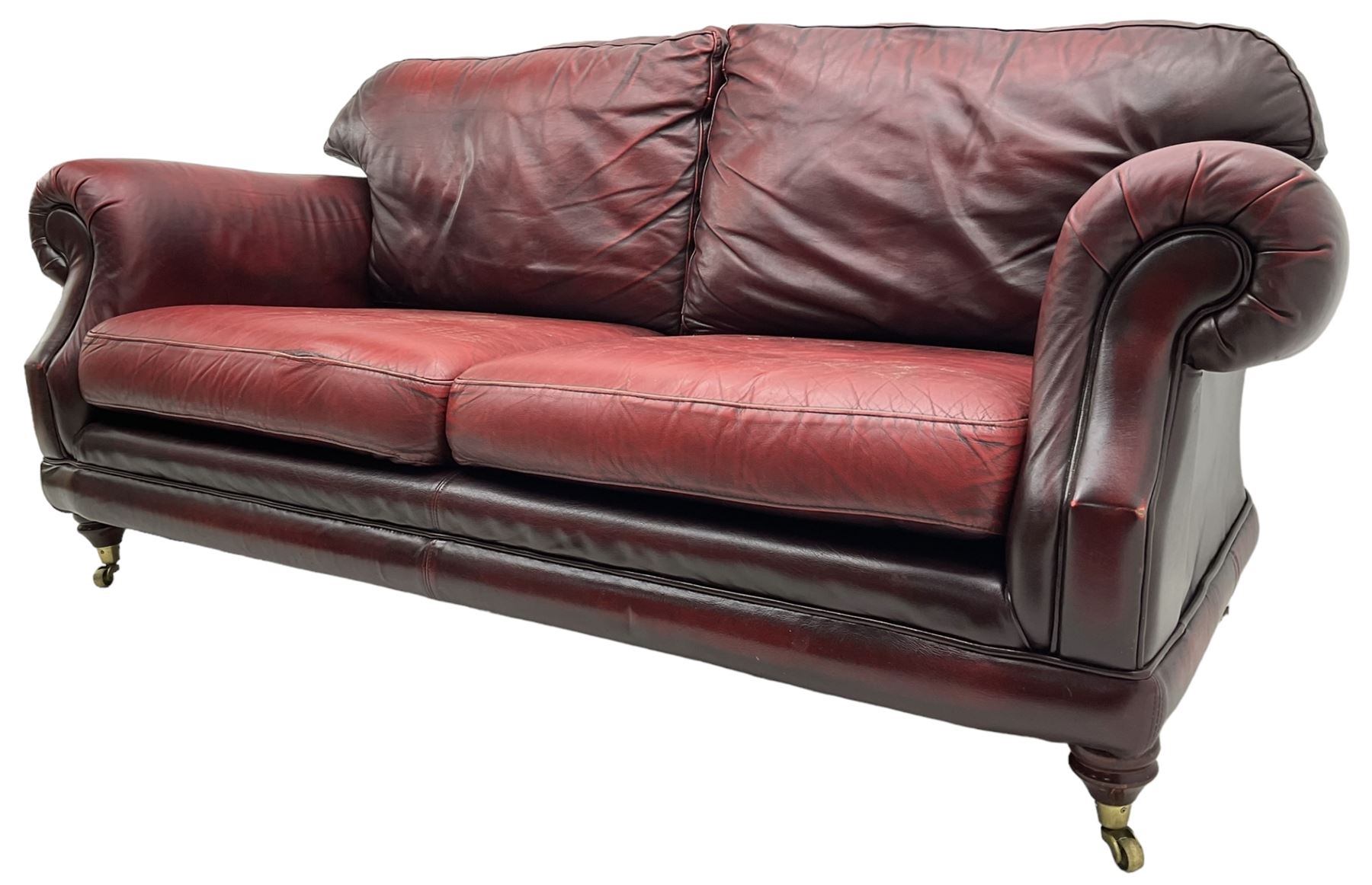 Thomas Lloyd - three-piece lounge suite, comprising of traditional shape two seat sofa (W190cm H80cm) and a pair of wingback armchairs (W100cm H91cm), each with rolled arms over turned supports with brass castors, upholstered in oxblood red leather