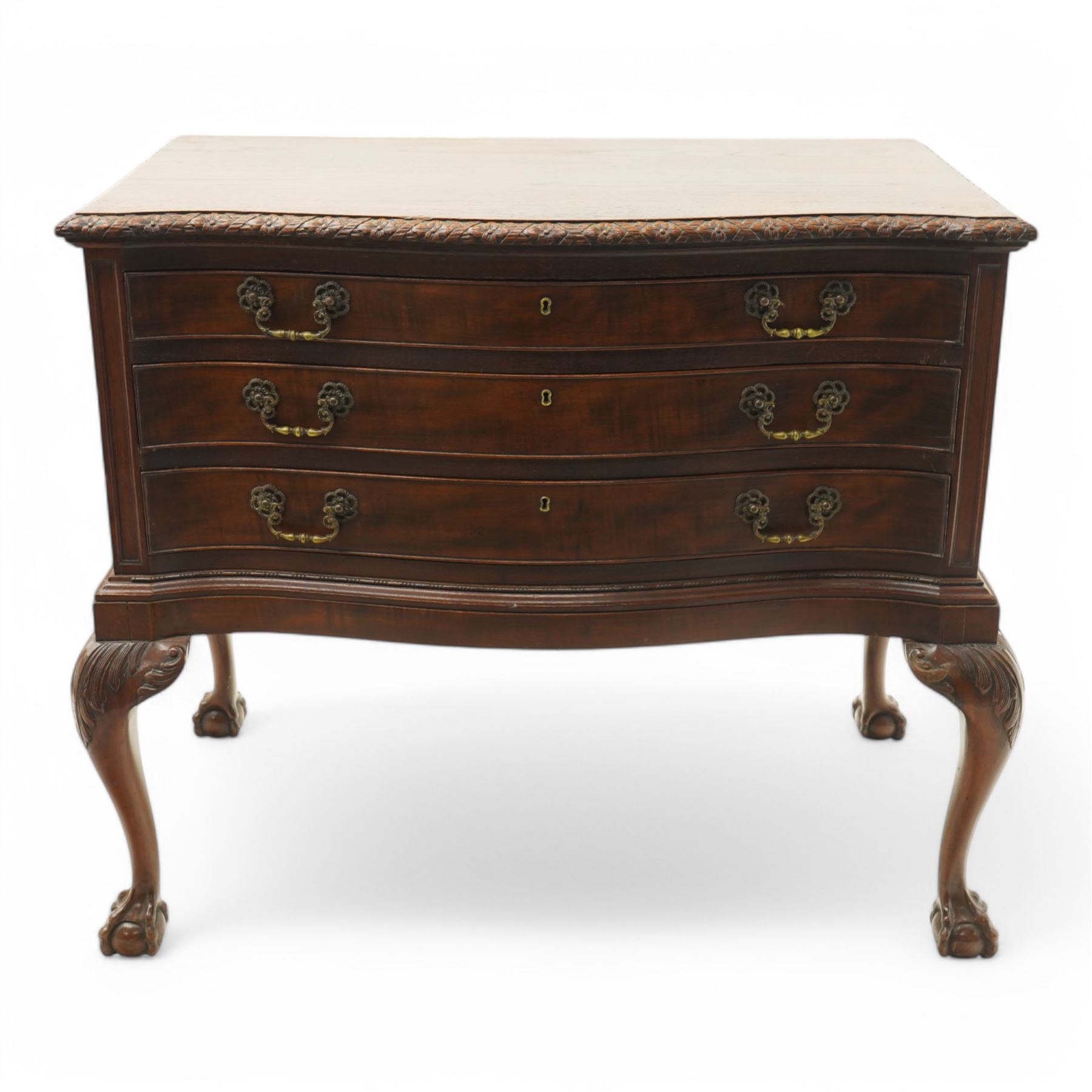 20th century oak and mahogany serpentine chest, the moulded top carved with trailing crossed ribbon and flower heads, fitted with three long cock-beaded drawers, ornate cast gilt metal handles, on acanthus leaf carved cabriole supports with ball and claw feet 