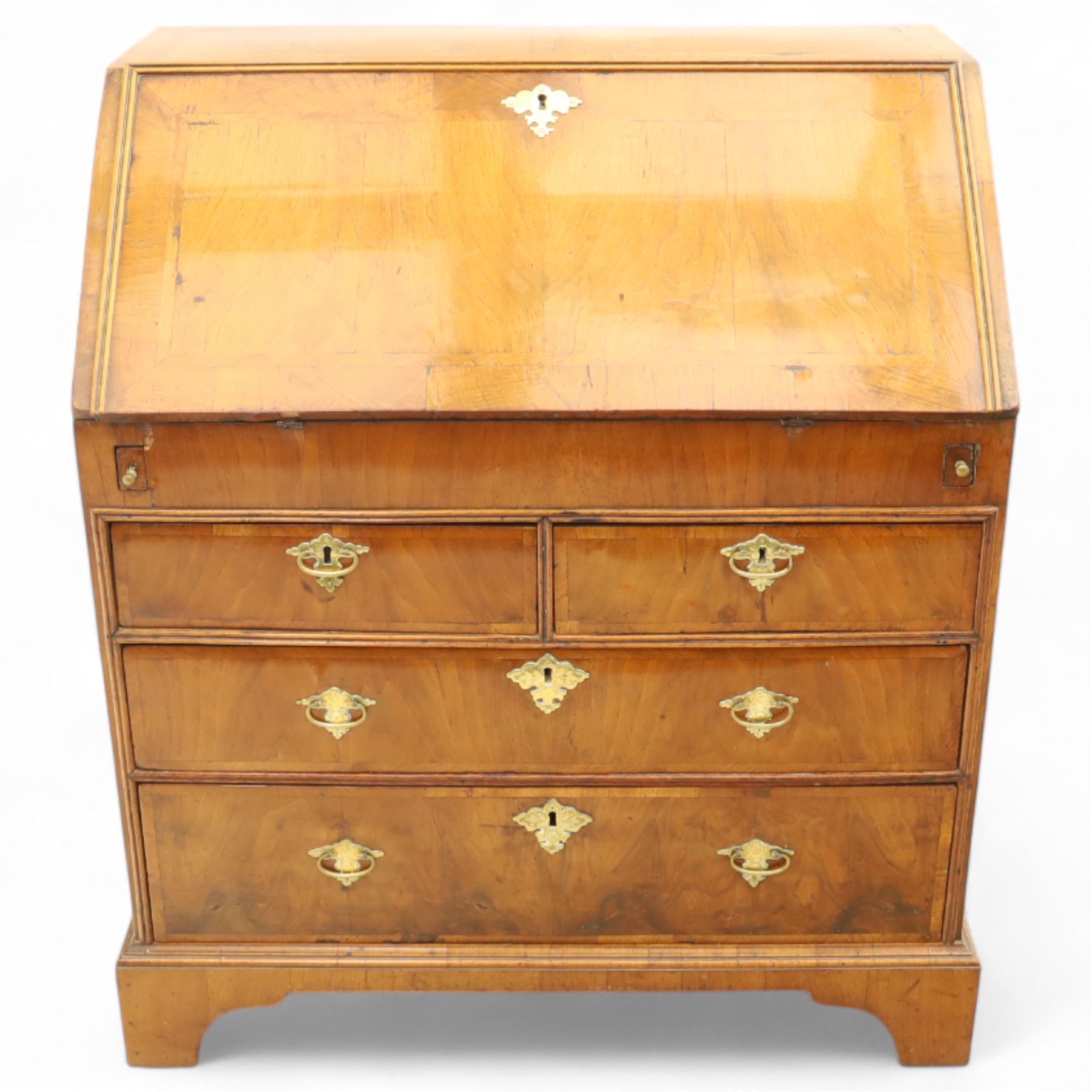18th century walnut and herringbone banded bureau, the fall front enclosing a stepped and arched interior fitted with pigeonholes, drawers and concealed compartments, green tooled leather writing surface, over two short and three long graduated drawers with brass escutcheons and bail handles, shaped bracket feet