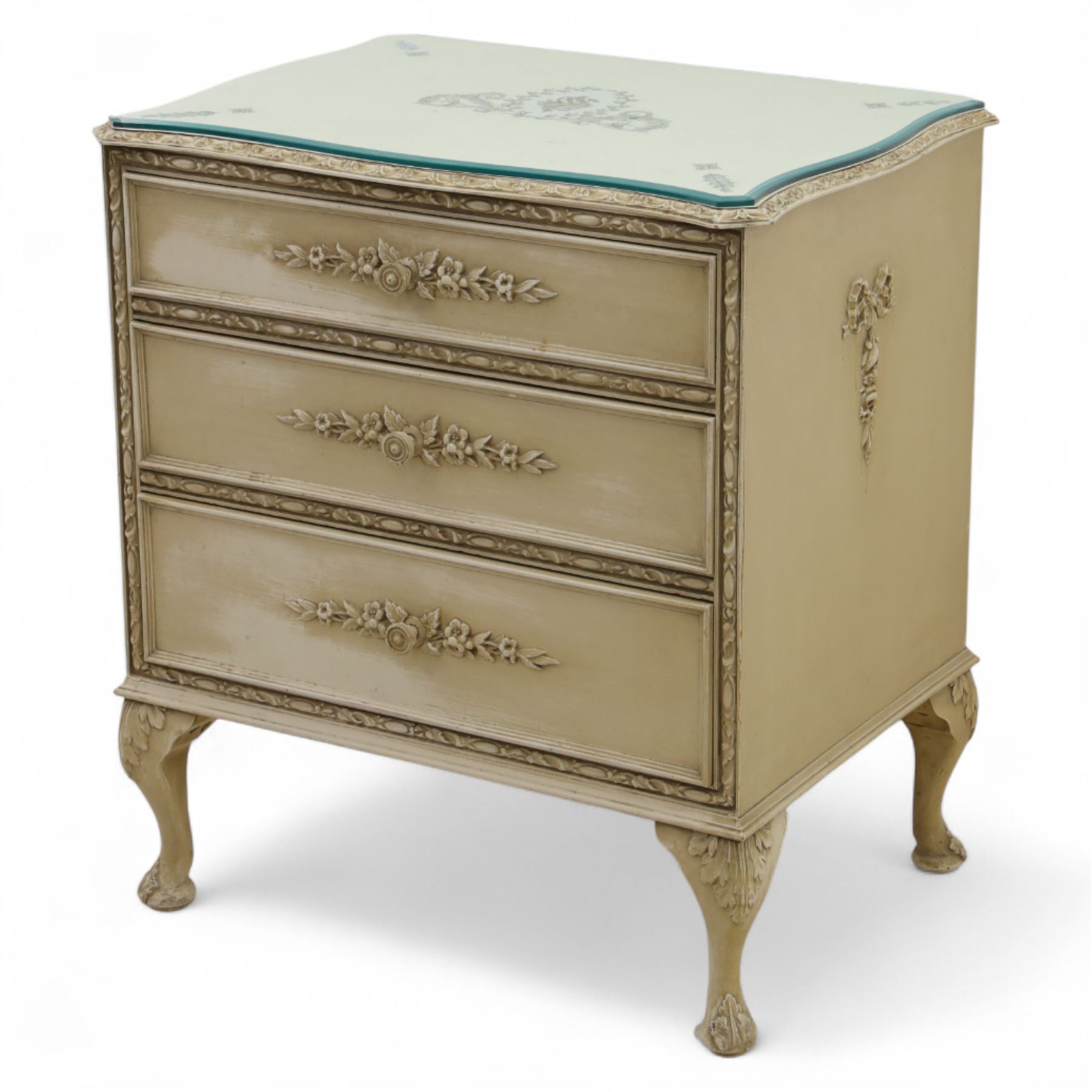 French design cream painted three drawer commode, shaped front with floral garland appliqués, fluted uprights and acanthus carved cabriole legs terminating in scroll feet
