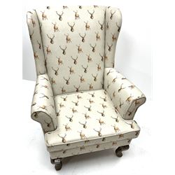 Wingback armchair upholstered in a grey fabric decorated with stags, cabriole feet, scrolling arms
