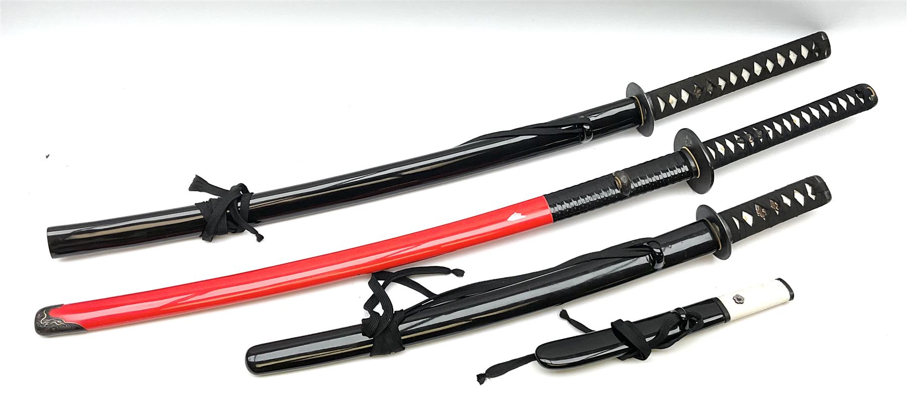 Reproduction Japanese sword daisho of katana and wakisashi with matching tanto; together with another reproduction katana; all with simulated fish skin grip and lacquered saya (4)