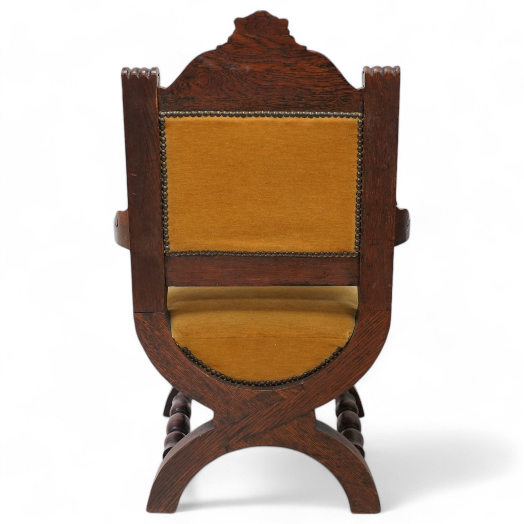 Victorian heavily carved oak X-framed throne chair, the cresting rail carved with mask and curling foliage, upholstered in mustard fabric, the arms and frame carved with scrolling foliage, united by turned stretchers 
