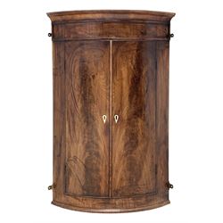 19th century bow front mahogany corner cupboard, projecting cornice over a plain frieze, figured and matched doors enclosing three shelves and two small drawers, W72cm, H111cm, D50cm

