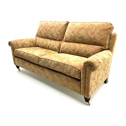 Duresta two seat sofa upholstered in a dark beige floral patterned fabric, raised on turned supports and castors 