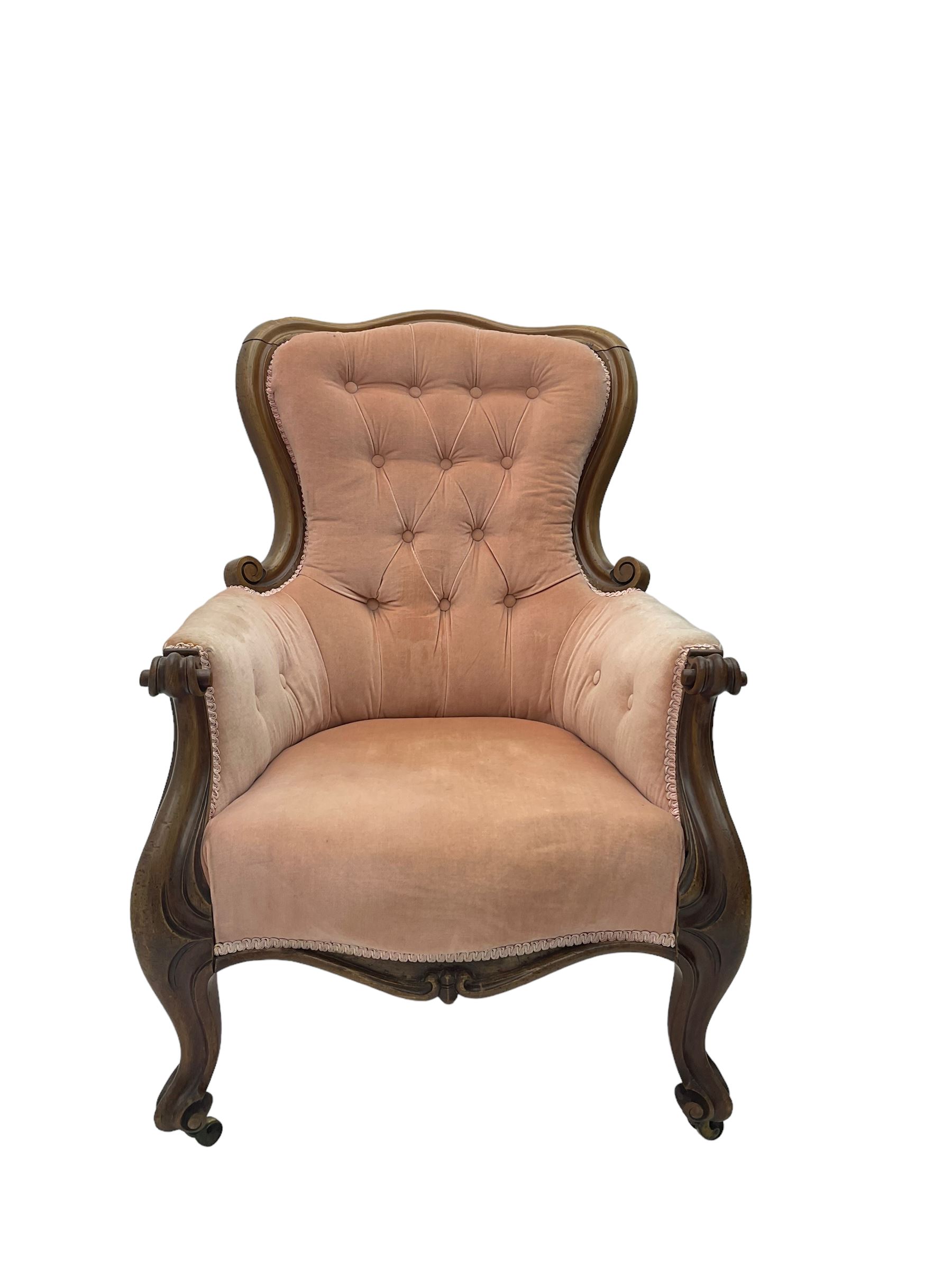 Victorian walnut framed armchair, shaped back with carved and scrolled arm terminals, upholstered in buttoned pale pink fabric, raised on cabriole supports terminating in castors