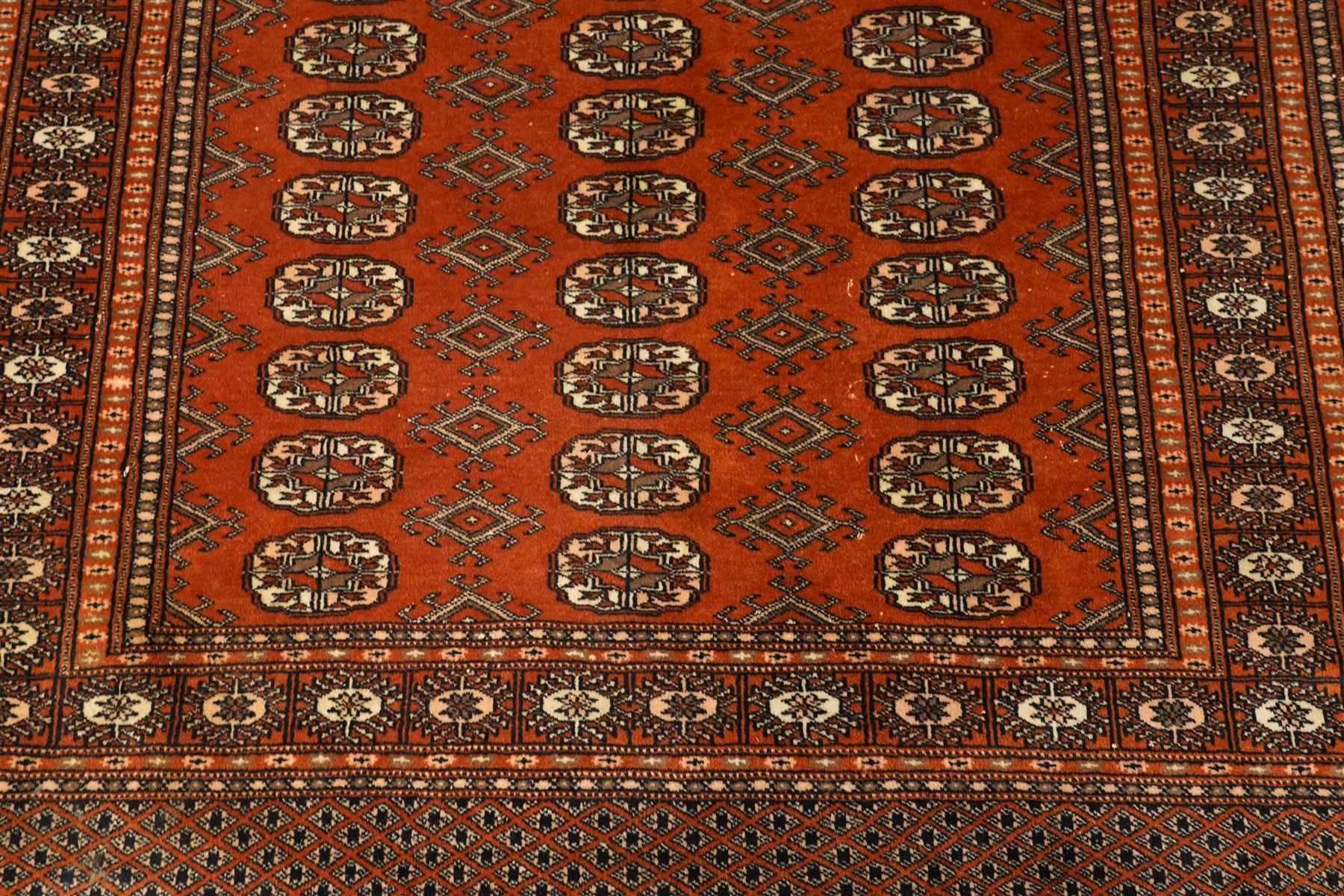 Bokhara hand-knotted carpet, terracotta ground with repeating rows of Tekke guls interspersed with geometric motifs, enclosed by multiple stylised floral and geometric borders, with fringed ends