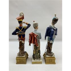 Group of seven Capodimonte figures of soldiers, to include four Bruno-Merli examples including Officer of the 12th Lancers 1820 and Captain of the 18th Hussars 1815, both raised upon ornate gilt plinths bearing British monarch motto in Latin 'Dieu et mon droit', and three further similar, all with crowned N mark beneath, tallest H32cm