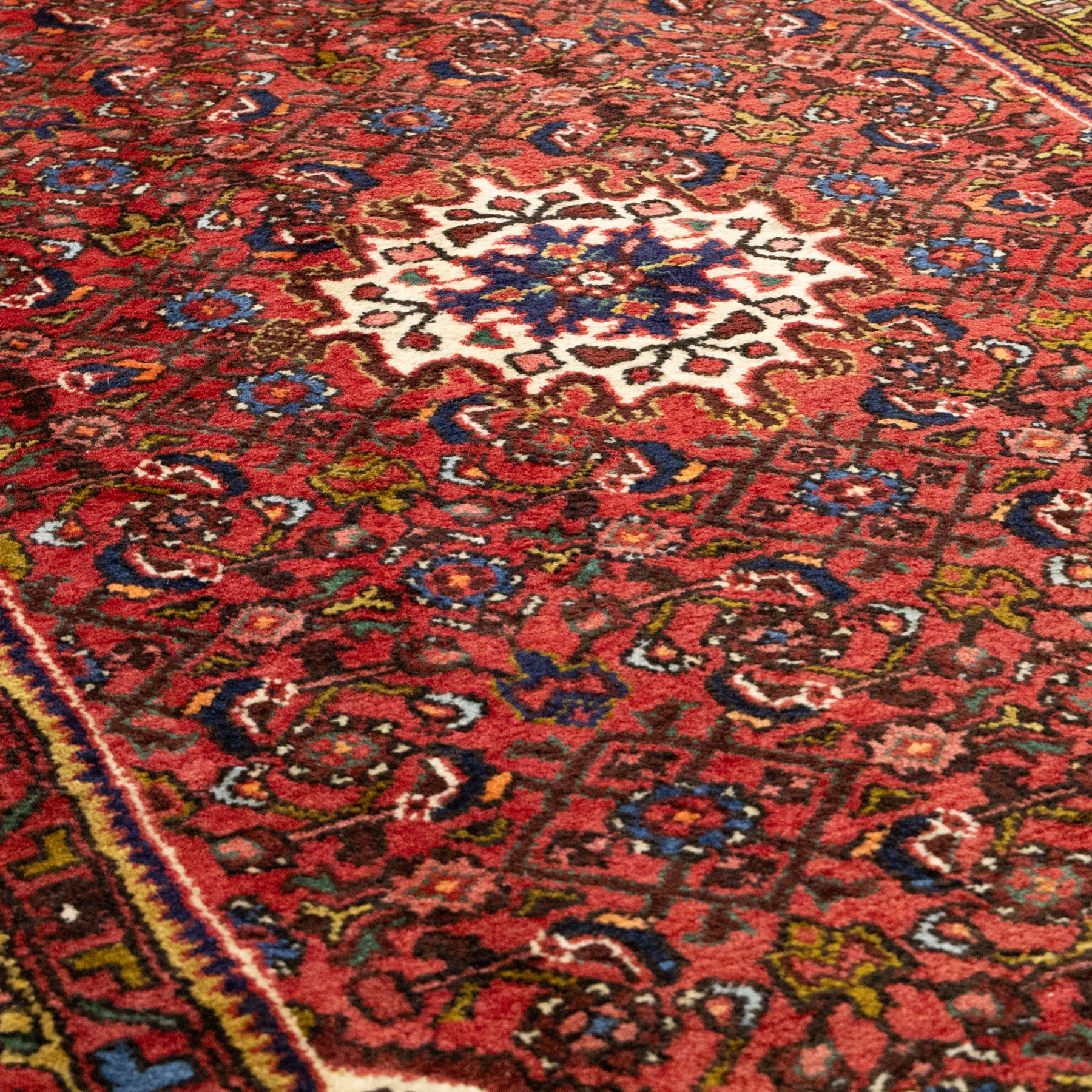 Hamadan hand-knotted rug, red field with small central floral medallion and dense repeating geometric motifs in dark blue, cream and green tones, within multiple patterned borders