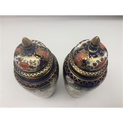 Pair of early 20th century Aynsley lidded vases, each painted with floral sprays, within deep blue and ornate gilt pattern borders, the conforming covers each with gilt finials, pattern no D141, both with printed marks beneath