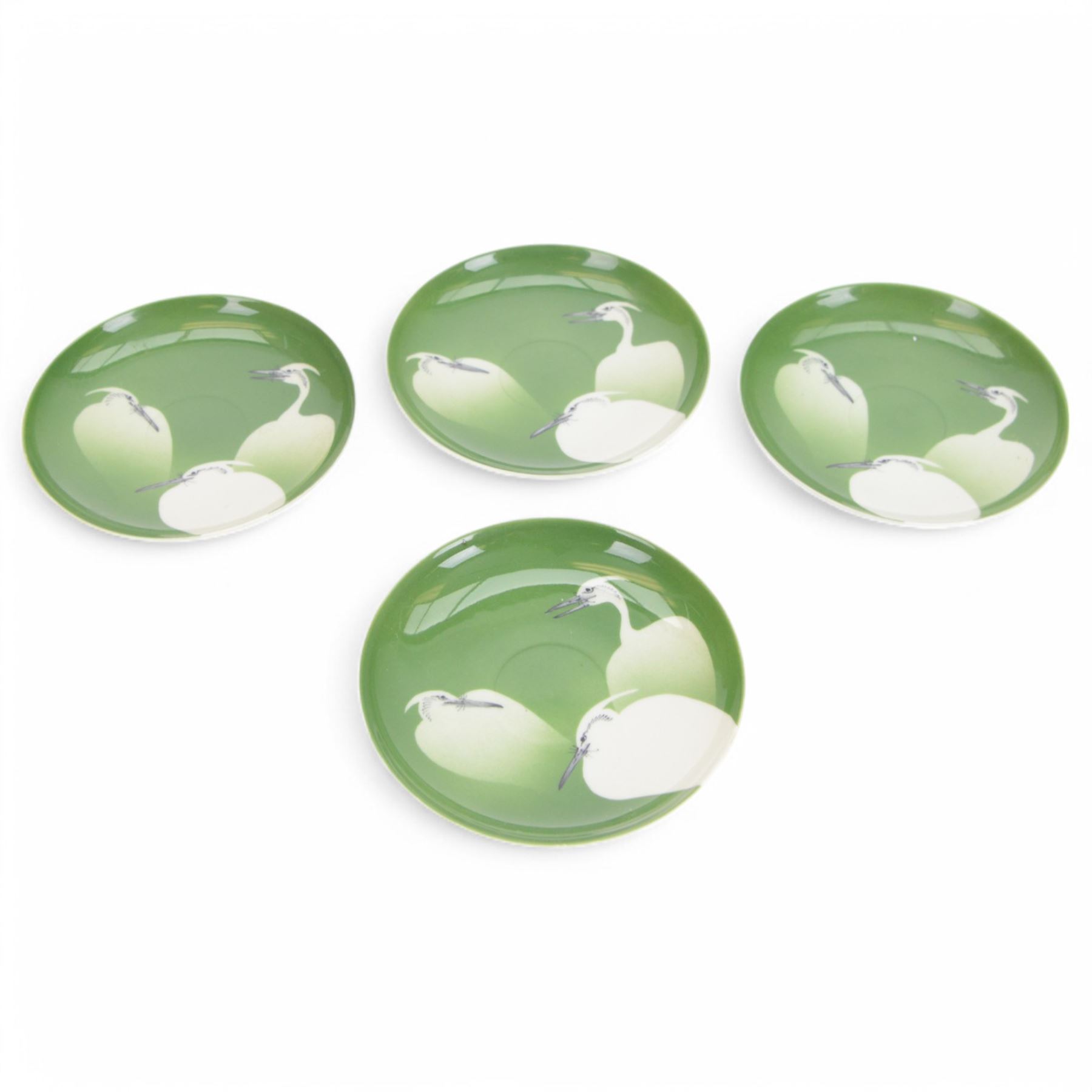 Nishiura Enji (1856-1914), two trio sets comprising tea cup, saucer and plate, with and two extra saucers and plate, decorated with herons upon a green ground and signed to the base, plates D19cm 