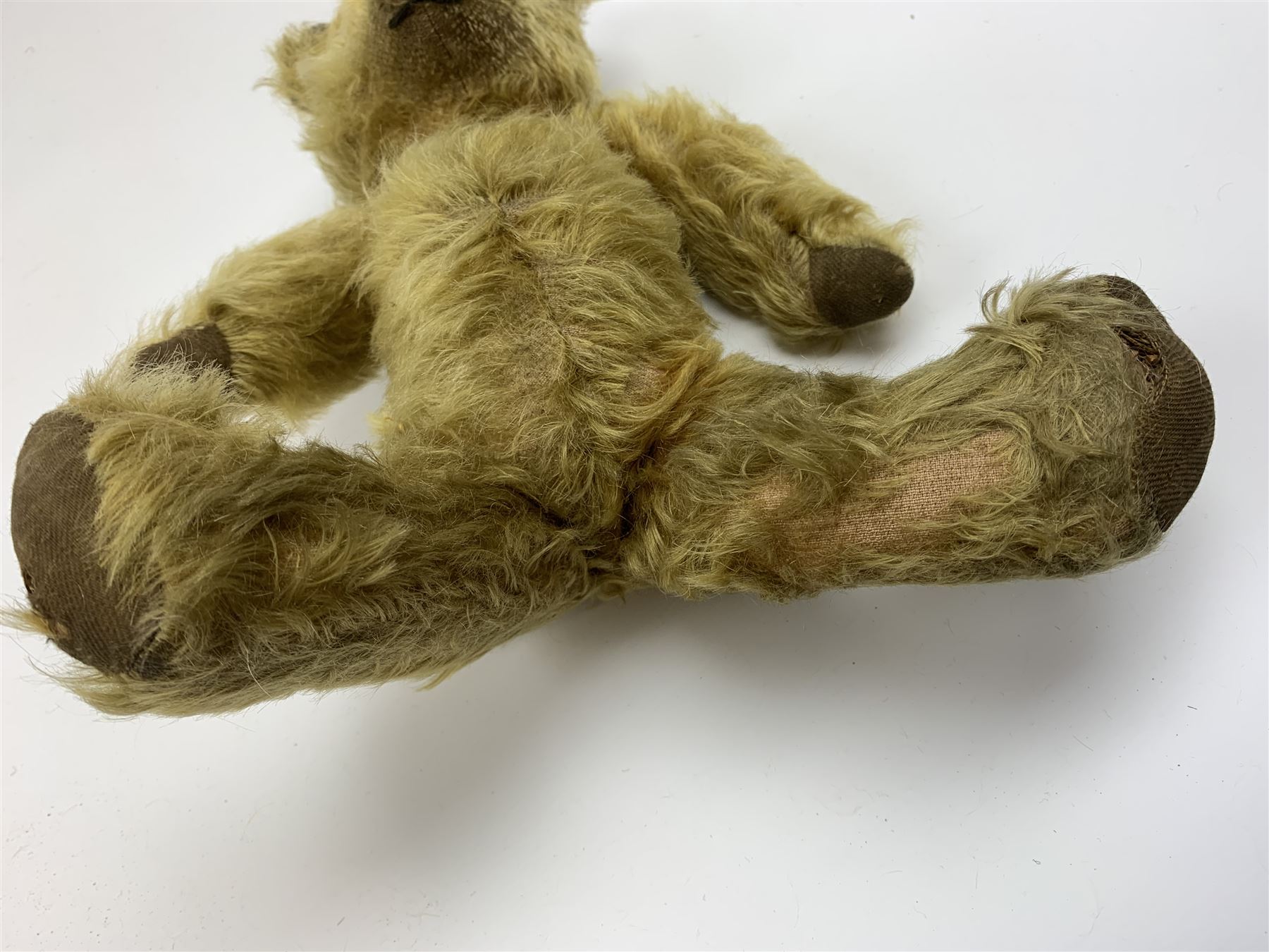 Early 20th century English teddy bear, WW1 period, with wood wool filled mohair body, fixed head with one boot button eye and vertically stitched nose and mouth and jointed limbs with cloth paw pads H16