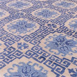 Late 20th century Chinese hand-woven wool carpet, ivory field with a lattice of stylized lotus medallions, contained within geometric key fret panels interspersed with a small floral device enclosed within a complementary Greek-Key border, the designs in tones of pale blue and soft cream