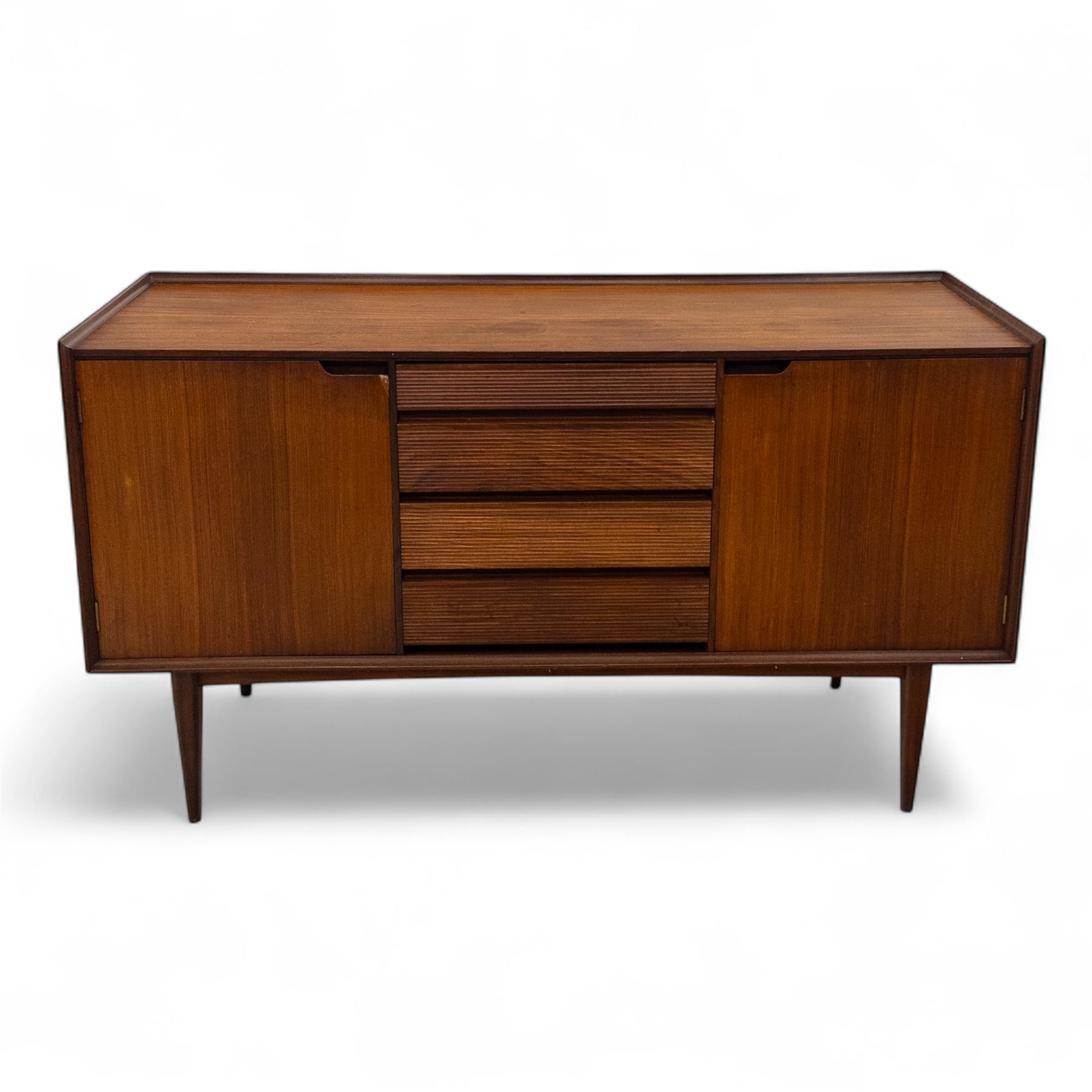 Richard Hornby for Fyne Ladye - mid-20th century afromosia teak sideboard, retailed by Heals of London, rectangular form, with low profile carved gallery lip, above three central drawers with ribbed drawer fronts, flanked by two cupboards with vertically grained doors and recessed pull handles, with streamlined moulded edges and sides, raised on tapered slender legs 