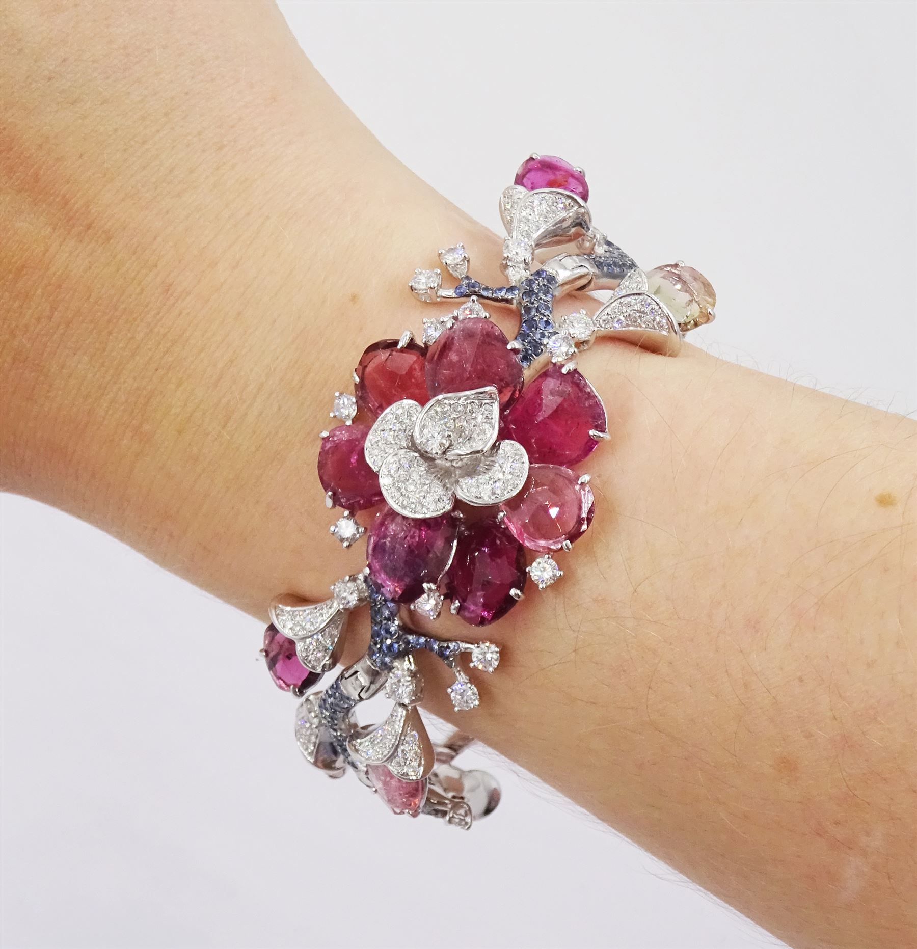18ct white gold gemstone set floral jewellery suite, comprising necklace, pair of earrings and bracelet, each with tourmaline flower petals, round brilliant cut diamond centres and sapphire stems, stamped