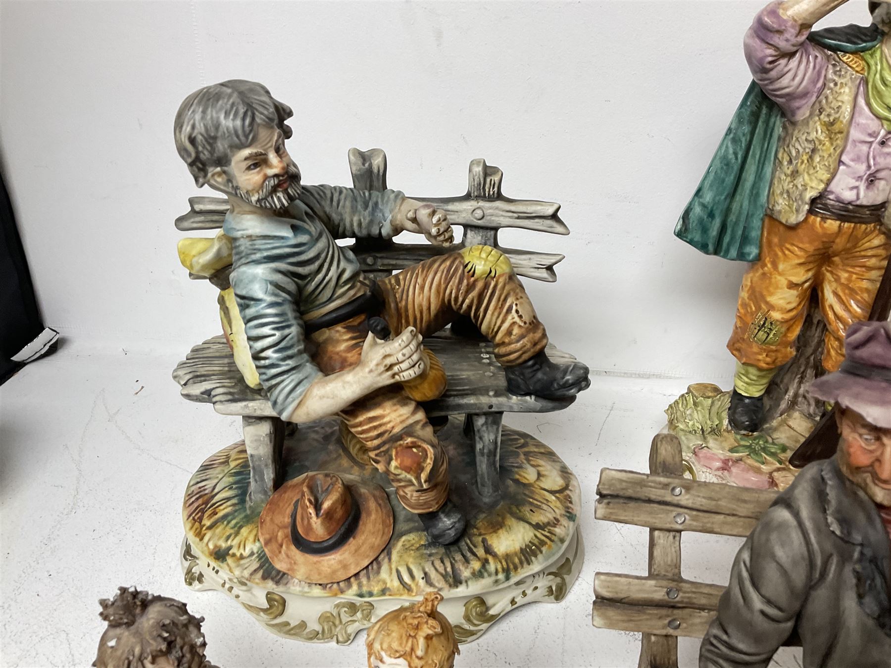 Group of Capodimonte figures, to include musical organ grinder with donkey and monkey, two tramp figures on benches, man with gun and choir boy and girl figures