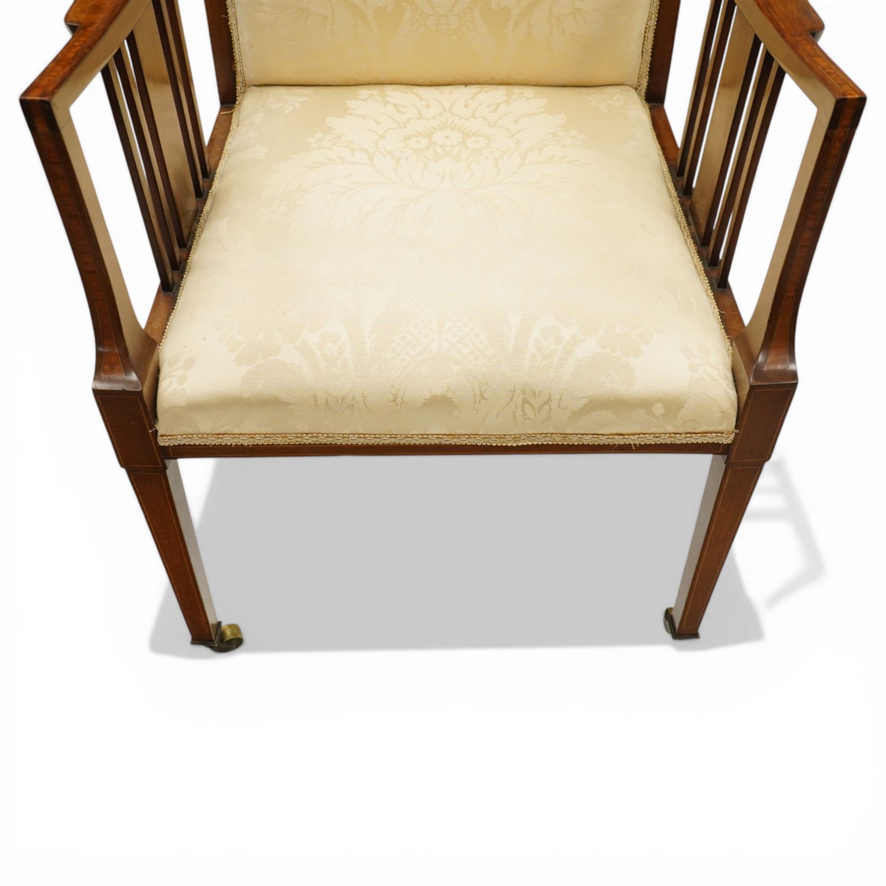 Arts & Crafts period inlaid mahogany framed armchair, swept arms with satinwood-strung supports over back and sprung seat upholstered in cream foliate damask fabric, on square tapering supports with castors