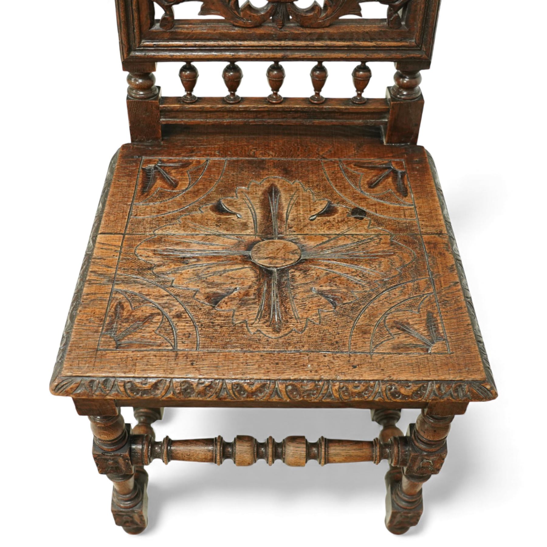 18th century carved oak hall chair, the rectangular pierced back carved with scrolling foliate ornament and central rosette beneath a shaped cresting, the boarded seat carved with stylised foliage, raised on turned legs united by stretchers