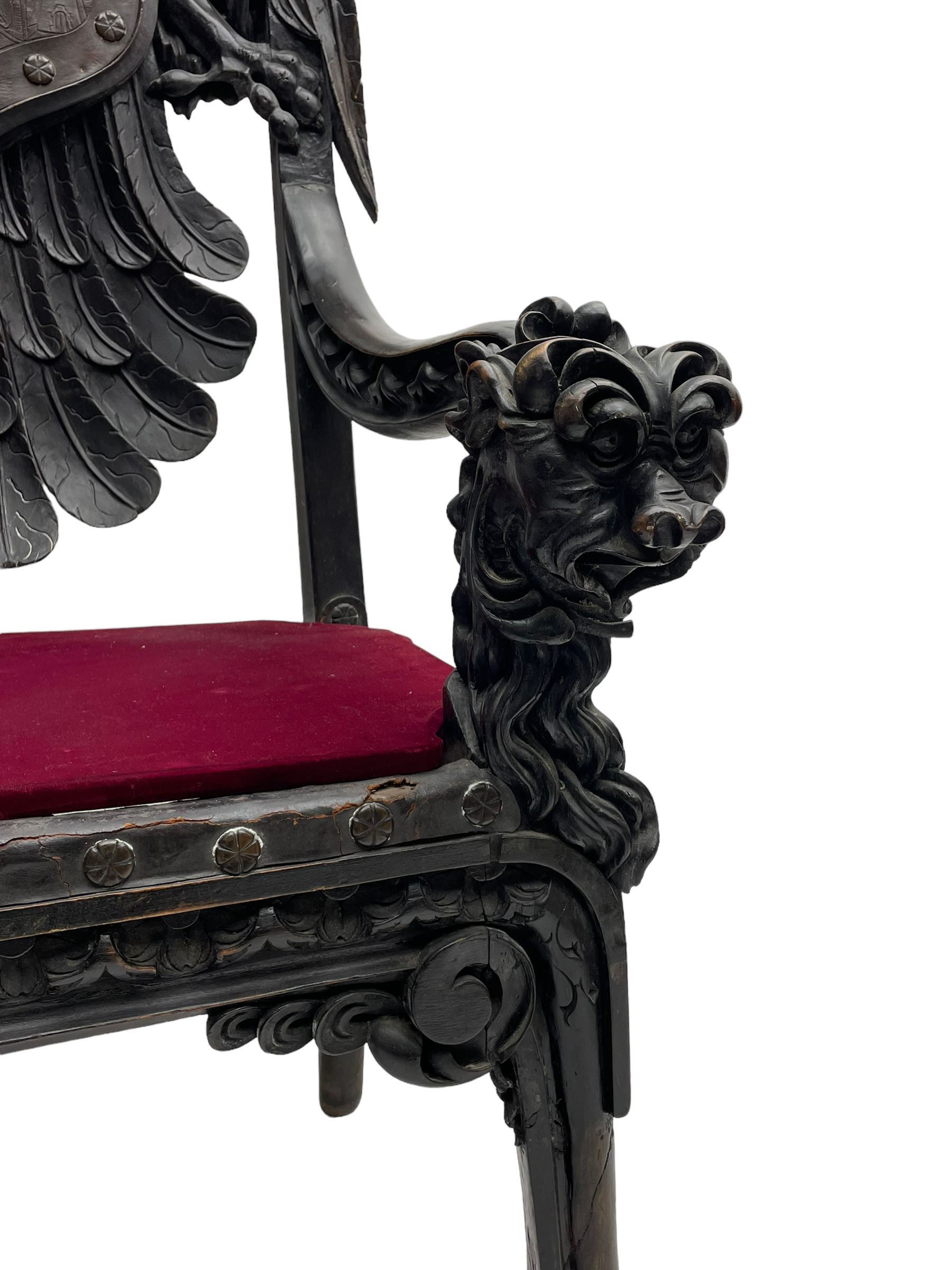 Grand mid-to-late 19th century heavily carved beech framed throne chair, the crown pediment carved with flower heads and cross finial, scroll and acanthus carved upright supports with twin perching griffin back enclosing etched leather work heraldic shield with castle and lion motifs over splayed feathers, flower head carved down sweeping arms with grotesque carved terminals, the seat rails carved with further flower heads on moulded supports with oversized ball and claw carved feet

Provenance: A very similar chair was used in the filming of Stanley Kubrick's 'Eyes Wide Shut' (1999)
