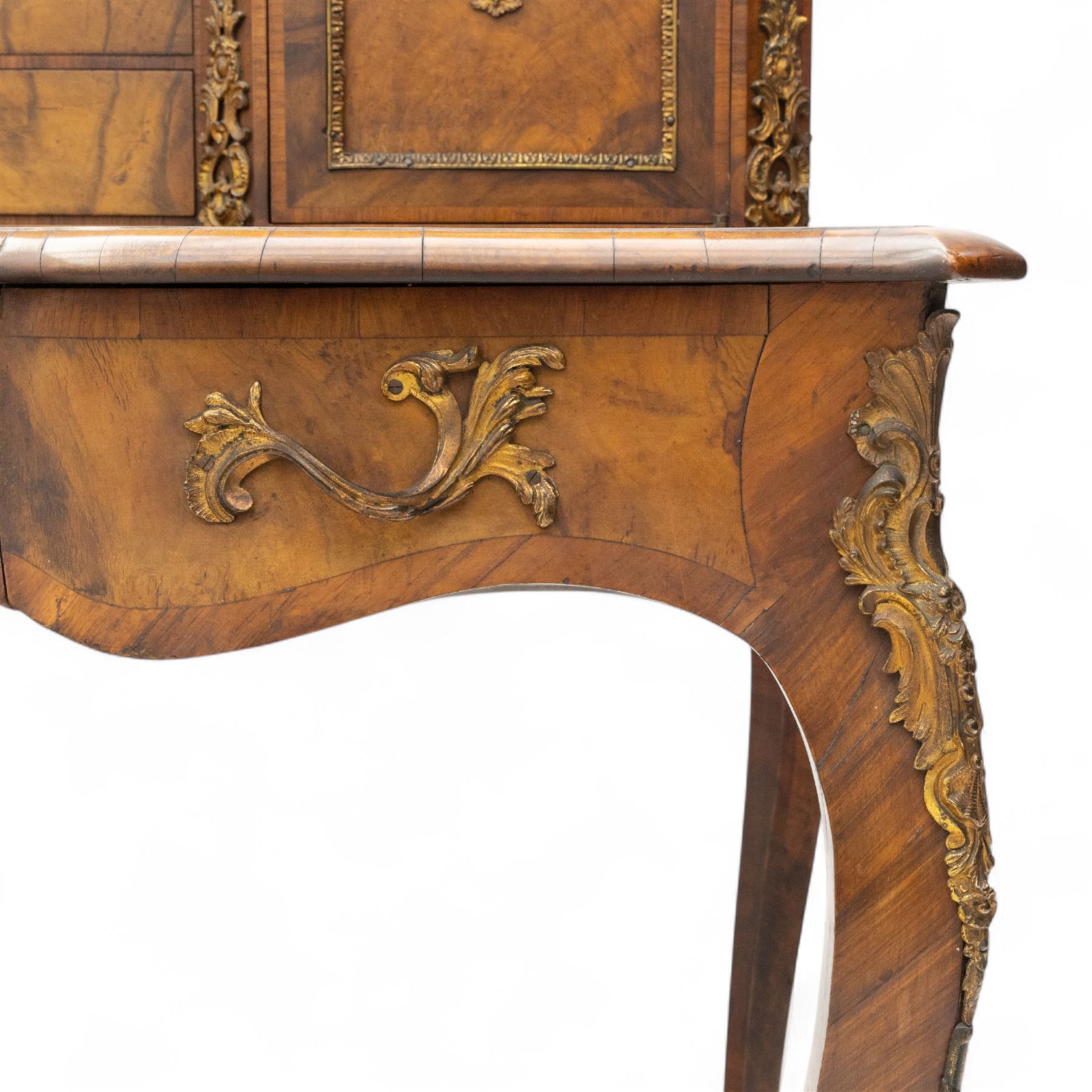 Late 19th-century Louis XV revival gilt bronze mounted and walnut Bonheur-de-Jour, rectangular-shaped serpentine form, with gilt bronze beading, frieze with two blind drawers and gilt bronze handles, centre drawer with large central serves style porcelain plaque, the elevated section with brass gallery above panelled cupboard doors also with serves style porcelain plaques and gilt bronze mounts, interior with single shelf, central section with four drawers each with gilt bronze handles, raised on slender cabriole legs fitted with gilt bronze rococo style masks and sabots