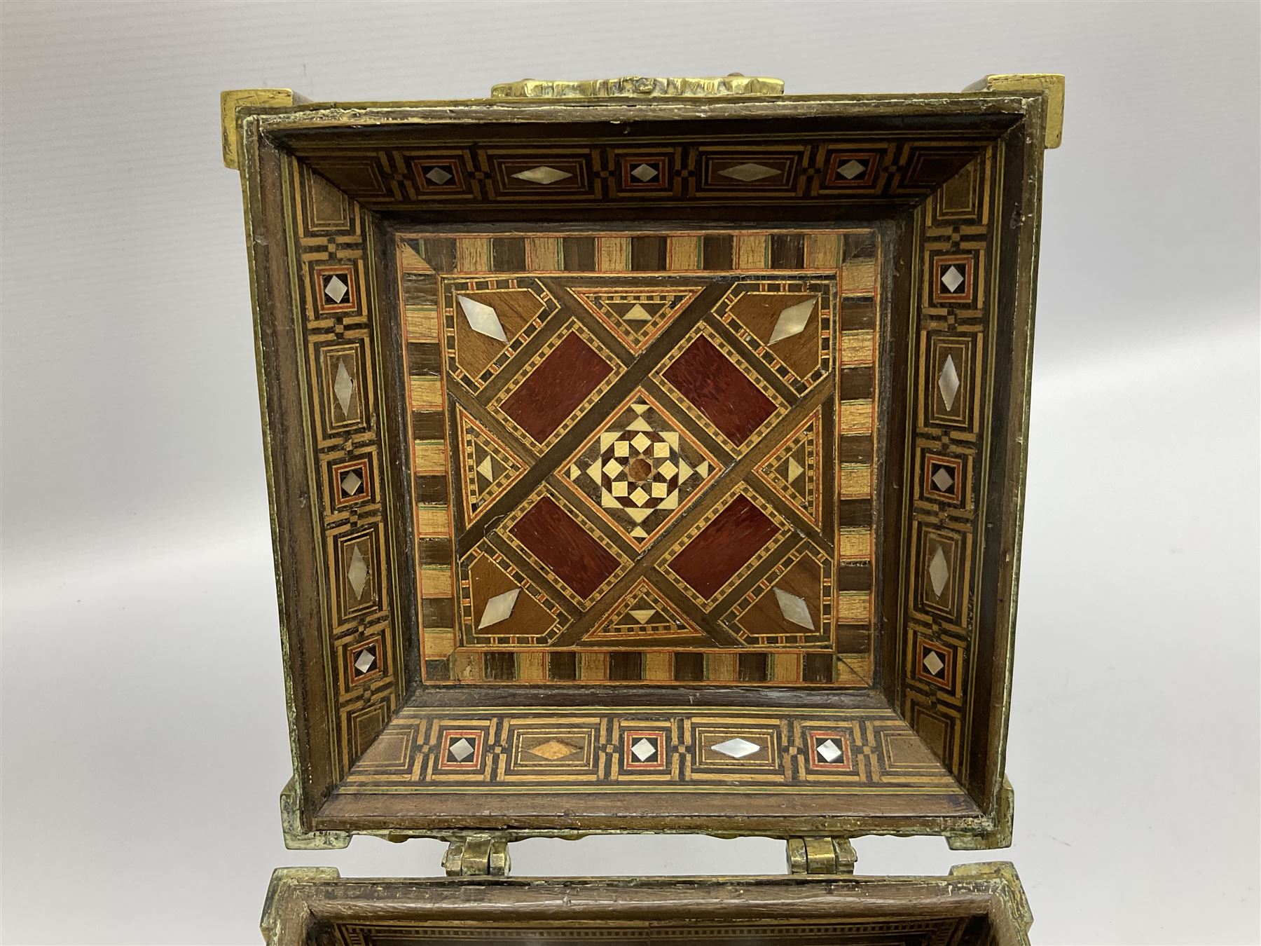 Late 19th century Damascus Cairoware Quran box, of square form with canted hinged cover, upon four circular pad feet, the brass exterior inlaid with silver and copper script and decorative detail, opening to reveal a marquetry lined interior, H15.5cm W19cm D19cm
