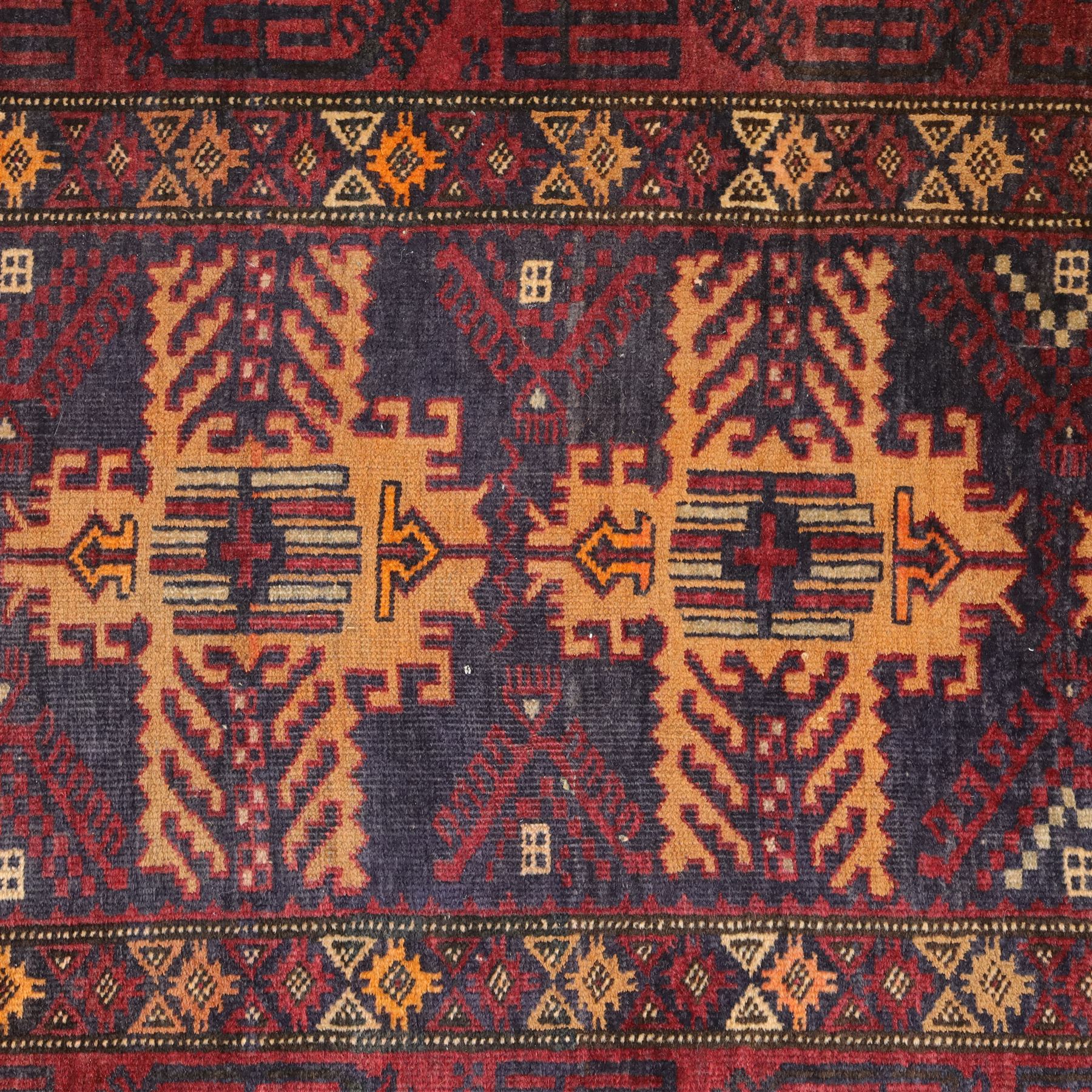 Baluch hand-knotted rug, deep red and indigo field decorated with a vertical arrangement of stylized geometric medallions within multiple narrow borders, 95x163cm, and Tekke Turkman rug, madder red field decorated with repeating rows of octagonal guls, framed by multiple geometric borders 84x129cm, (2)