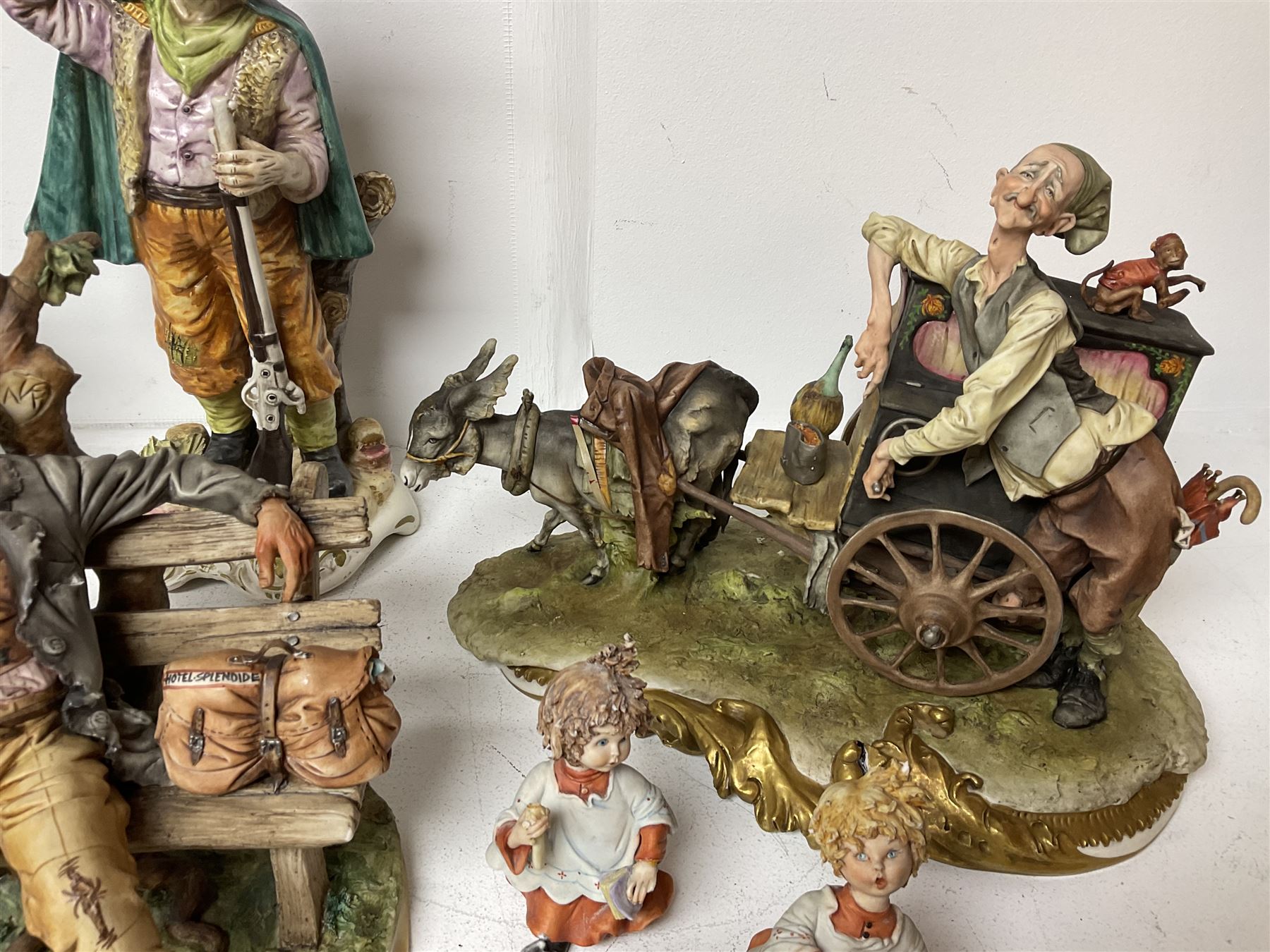 Group of Capodimonte figures, to include musical organ grinder with donkey and monkey, two tramp figures on benches, man with gun and choir boy and girl figures