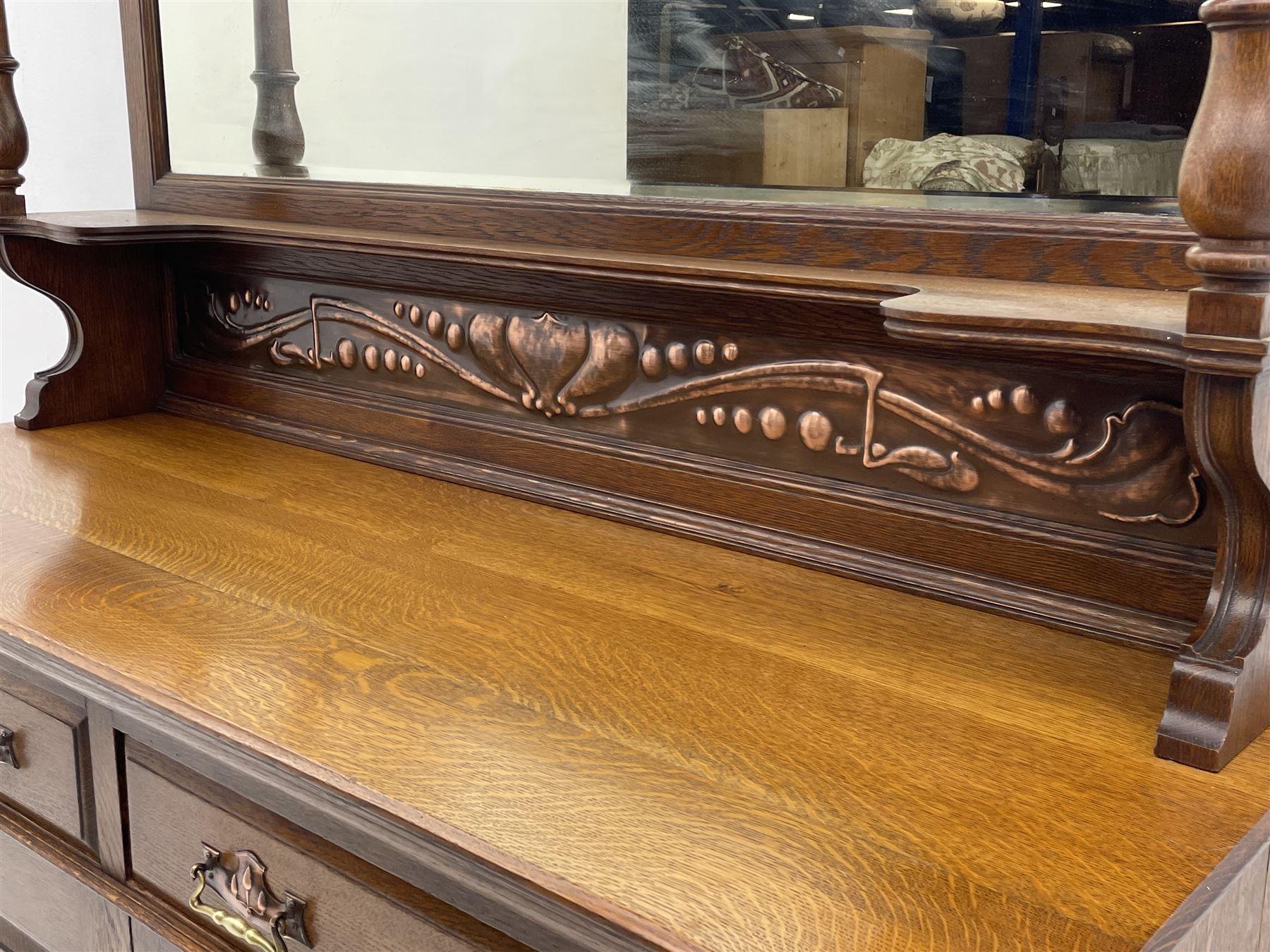Arts and Crafts period oak mirror back dresser, projecting cornice above rectangular bevelled mirror and shelf, two turned supports, inset copper panel with embossed decoration, rectangular moulded top over two drawers and two panelled cupboard, moulded plinth base, brass and copper strappings and handles 