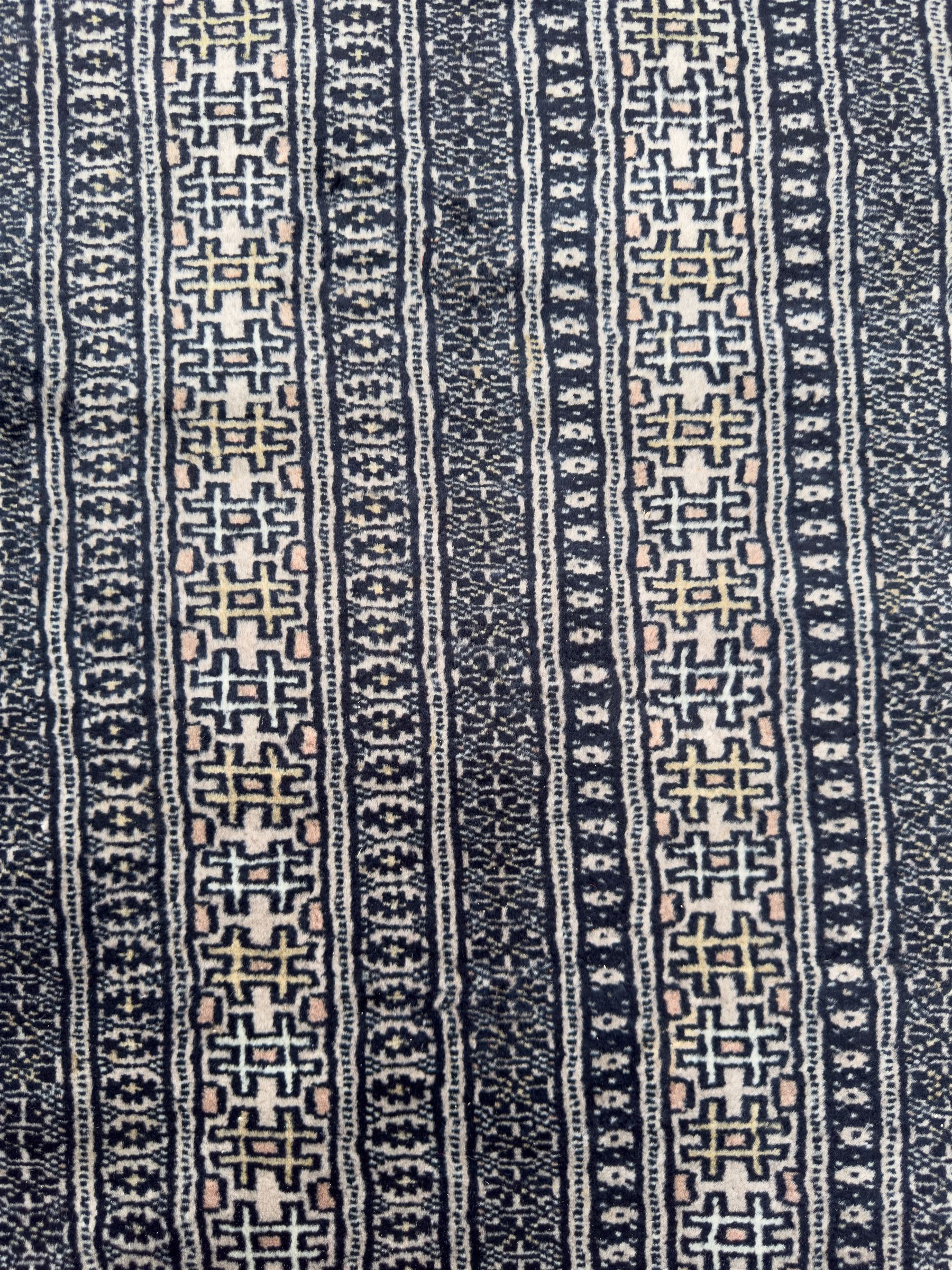 Large Persian Bokhara wool rug, the field decorated with repeating gul motifs in lozenge medallions across a dark ground, enclosed by multiple geometric borders in indigo, ivory and terracotta, from the region of Baluchistan