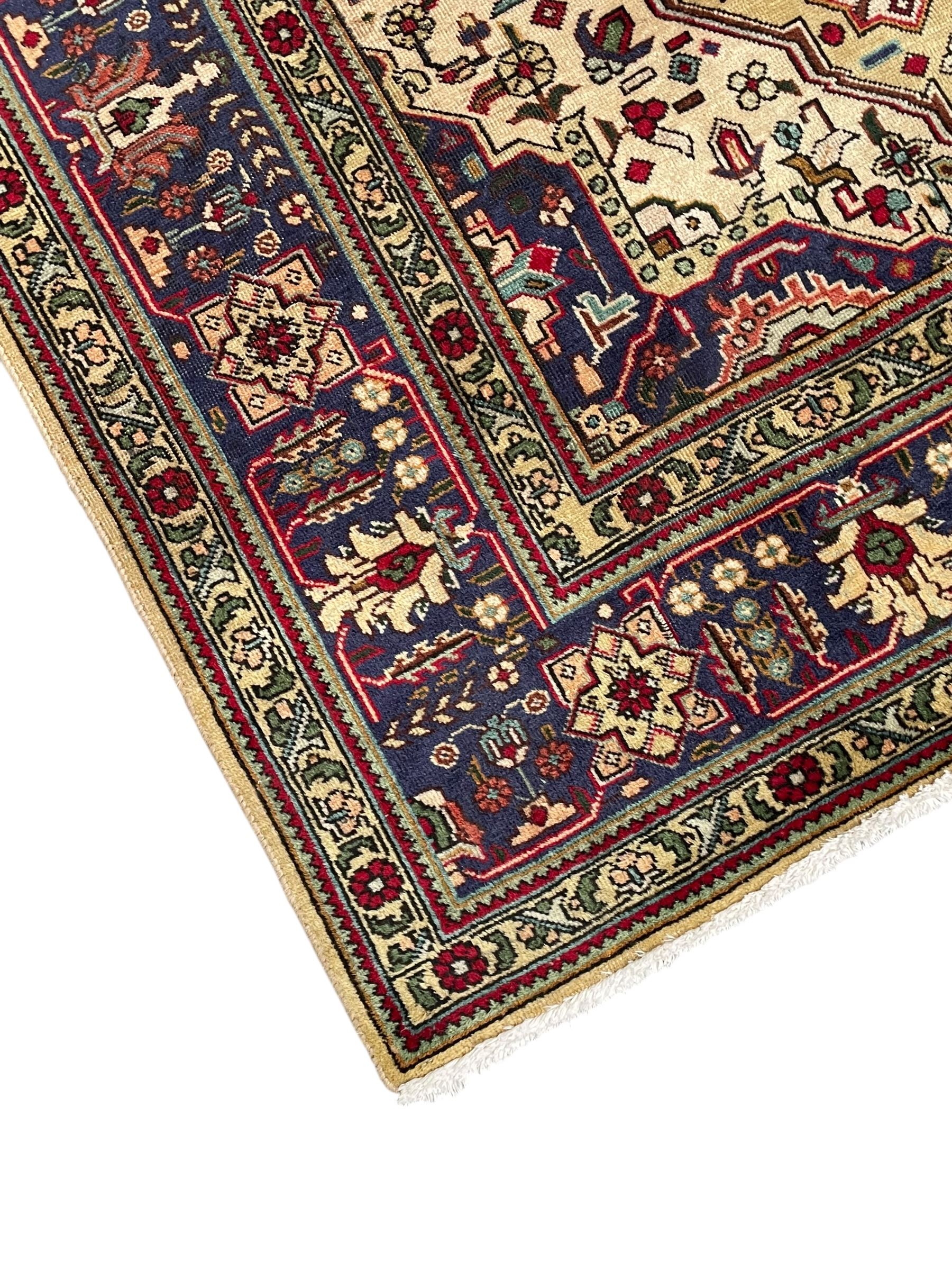Persian Heriz pale wheat ground rug, indigo pole medallion surrounded by neatly arranged Hac and stylised flower head motifs, indigo main border decorated with alternating palmette motifs, within floral pattern guard stripes 