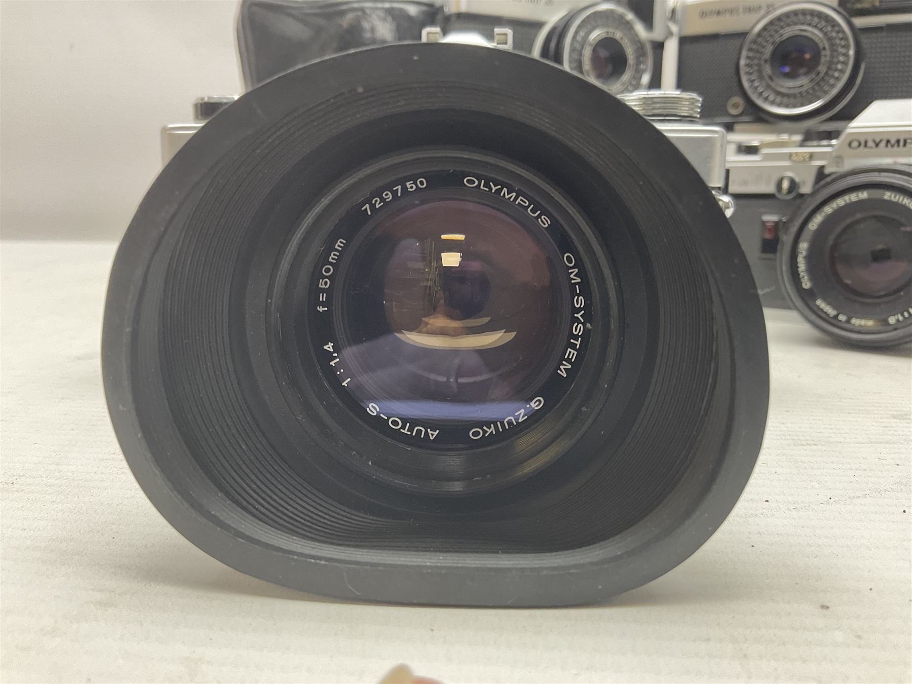 Four Olympus camera bodies, including Olympus OM10, serial no 20744269, with 'Olympus OM-System Zuiko Auto-S 50mm 1:1.8' lens serial no 3633644, Olympus OM-2 camera body serial no 460280 with 'Olympus OM-System G.Zuiko Auto-s 1:1.4 f=50mm' lens, serial no 729750, etc 