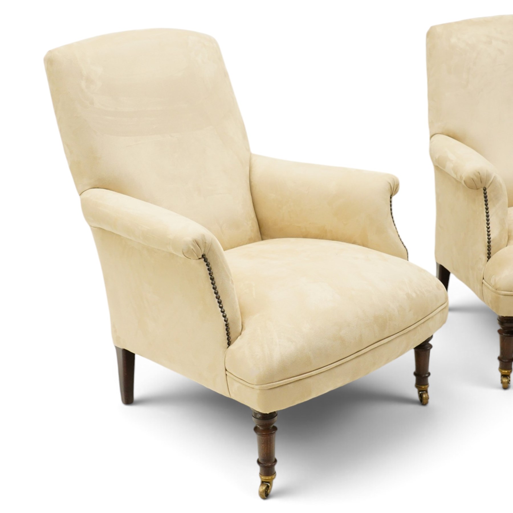 Sofas & Stuff - pair of ‘Thistle’ armchairs upholstered in neutral fabric, each with gently sloping back, padded scroll arms with close-set stud detailing, loose seat cushions, raised on turned wooden legs with brass castors