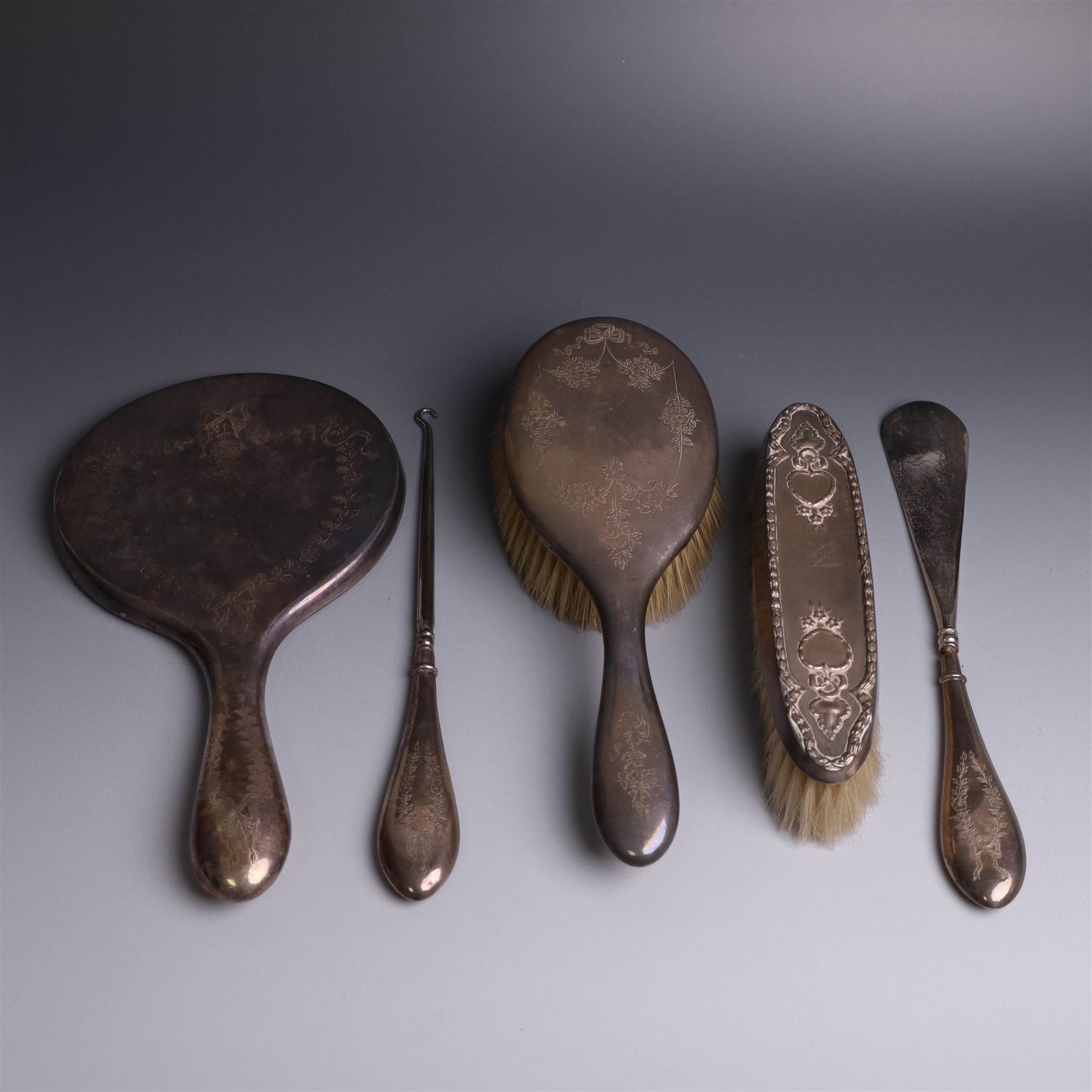 Early 20th Century silver mounted dressing table set, comprising hand mirror, shoe horn and a button hook, each with engraved floral decoration, together with a silver mounted hairbrush and clothes brush, all hallmarked