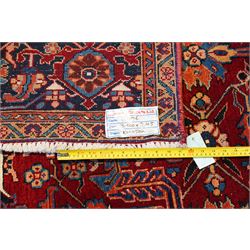 North West Persian Karadja hand-knotted carpet, deep red field decorated with an all-over lattice design of elongated geometric devices interspersed with rosettes and angular palmettes, enclosed by a dark indigo main border of stylized floral and geometric motifs between multiple guard stripes, with cotton fringe ends 
