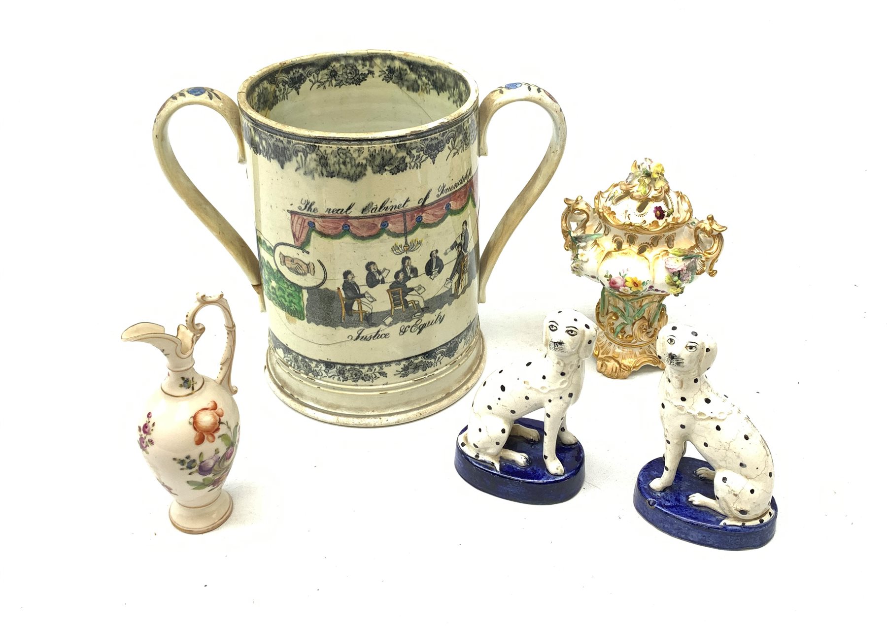 A large 19th century Staffordshire loving cup, detailed 'The Real Cabinet of Friendship Justice and Equity' (a/f), H22cm, together with a pair of 19th century Staffordshire dalmatians, upon oval blue bases, H13cm, a Dresden ewer hand painted with floral sprays, with mark beneath, H15.5cm, and a Coalbrookdale style floral encrusted vase and cover, H16.5cm. 
