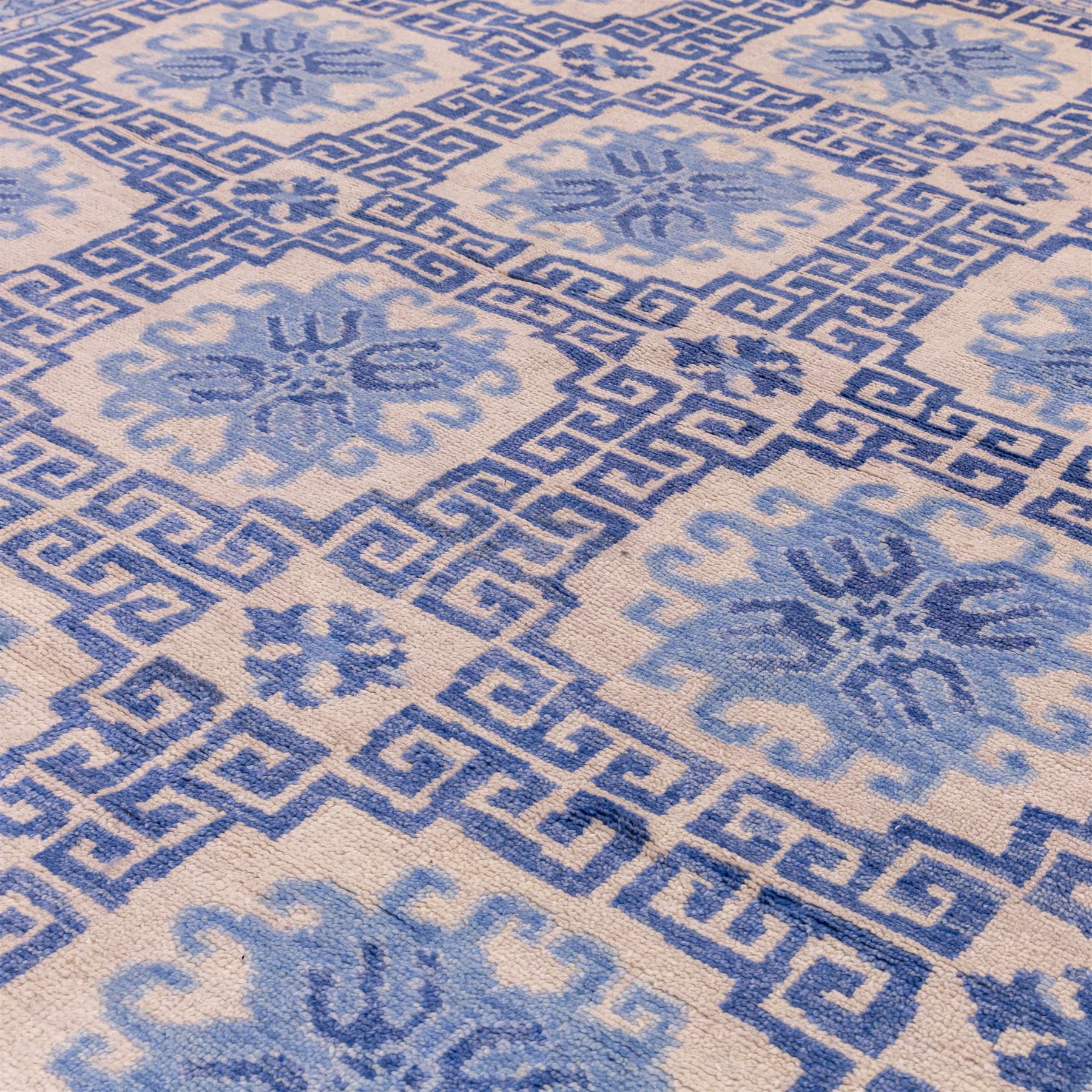 Late 20th century Chinese hand-woven wool carpet, ivory field with a lattice of stylized lotus medallions, contained within geometric key fret panels interspersed with a small floral device enclosed within a complementary Greek-Key border, the designs in tones of pale blue and soft cream